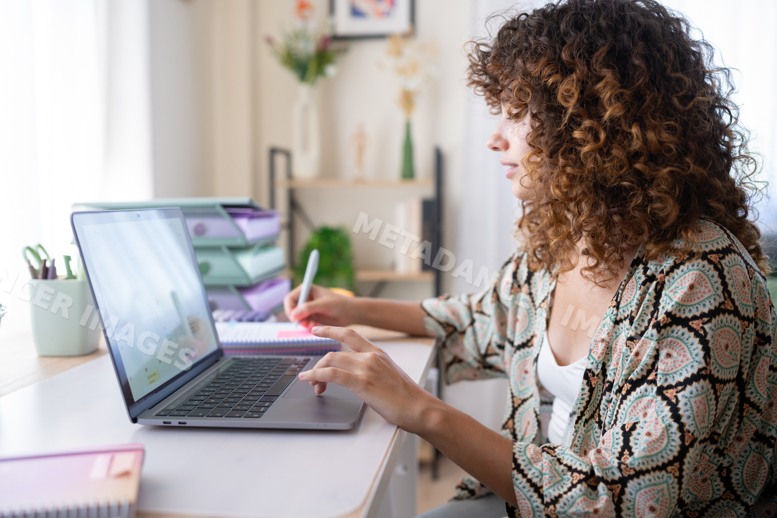White woman working on laptop and writing at home office desk