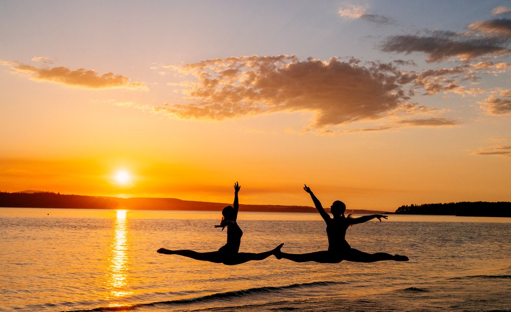Two white people performing yoga partner acrobatics leaps