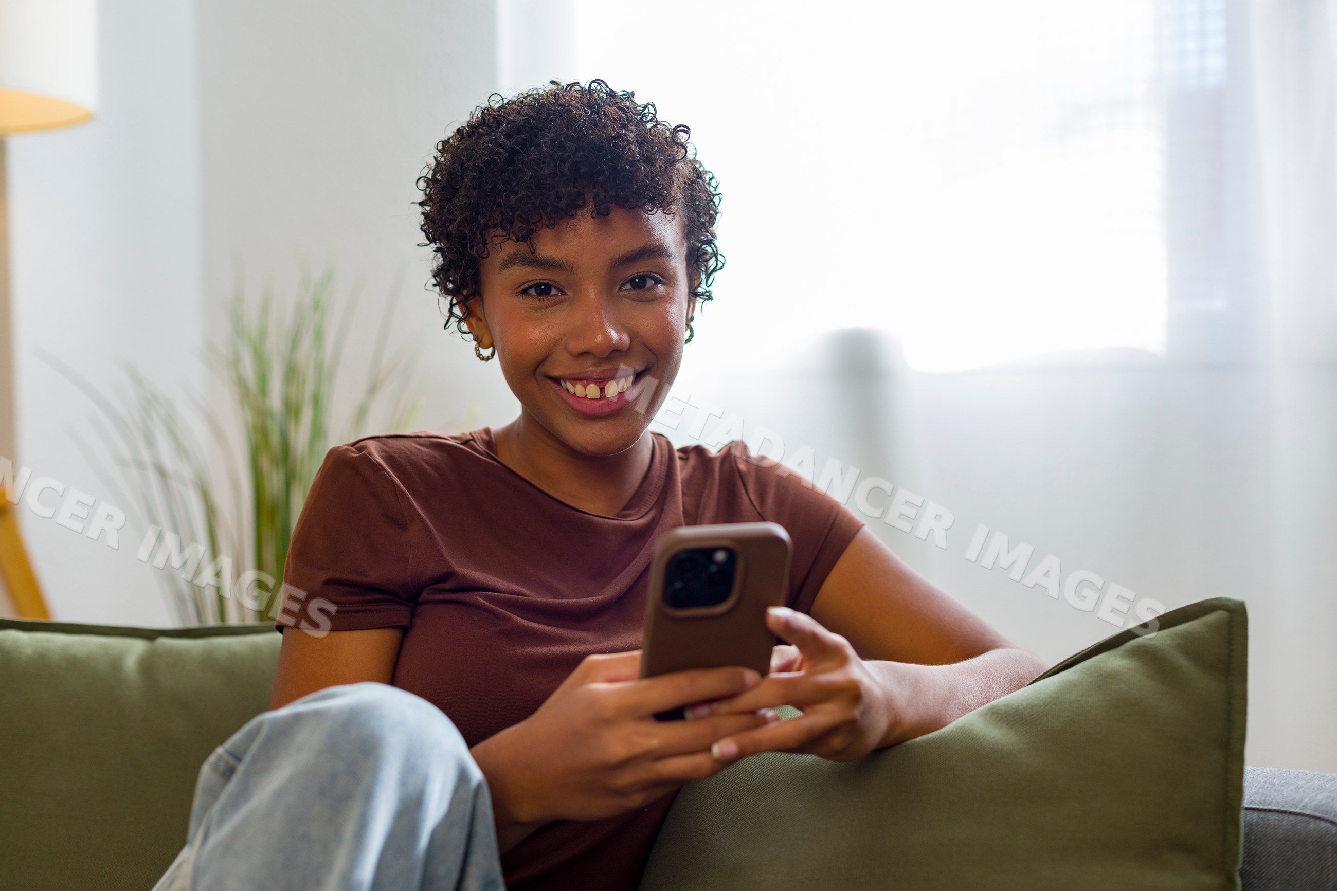 Young African American woman smiling and using smartphone on couch