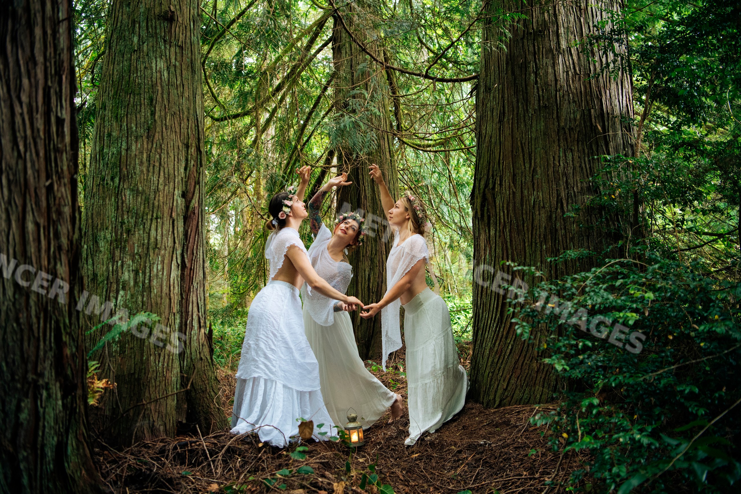 Three women dancing in white dresses with flower crowns in forest