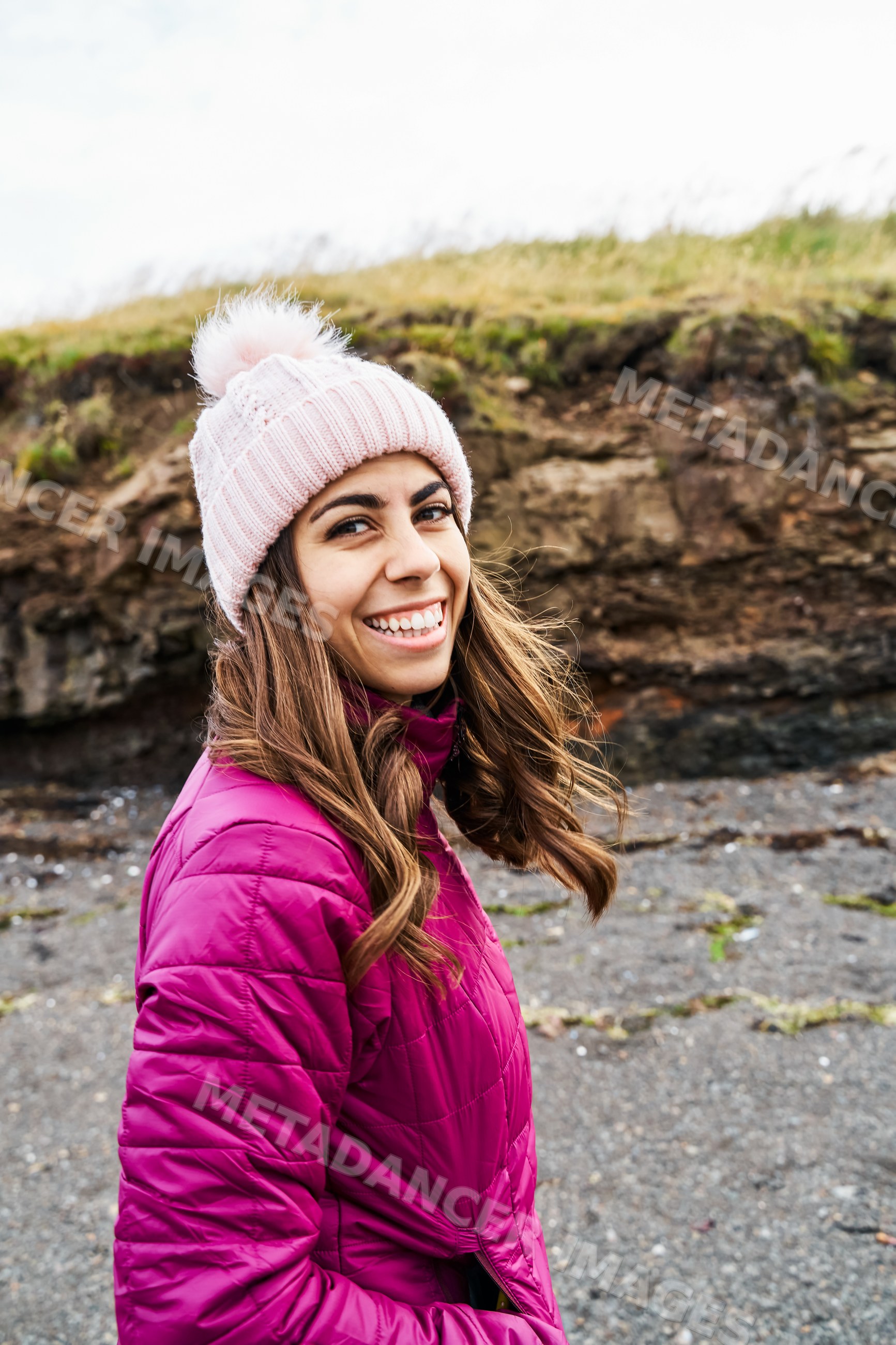 A smiling young woman wearing a pink winter hat and jacket outdoors