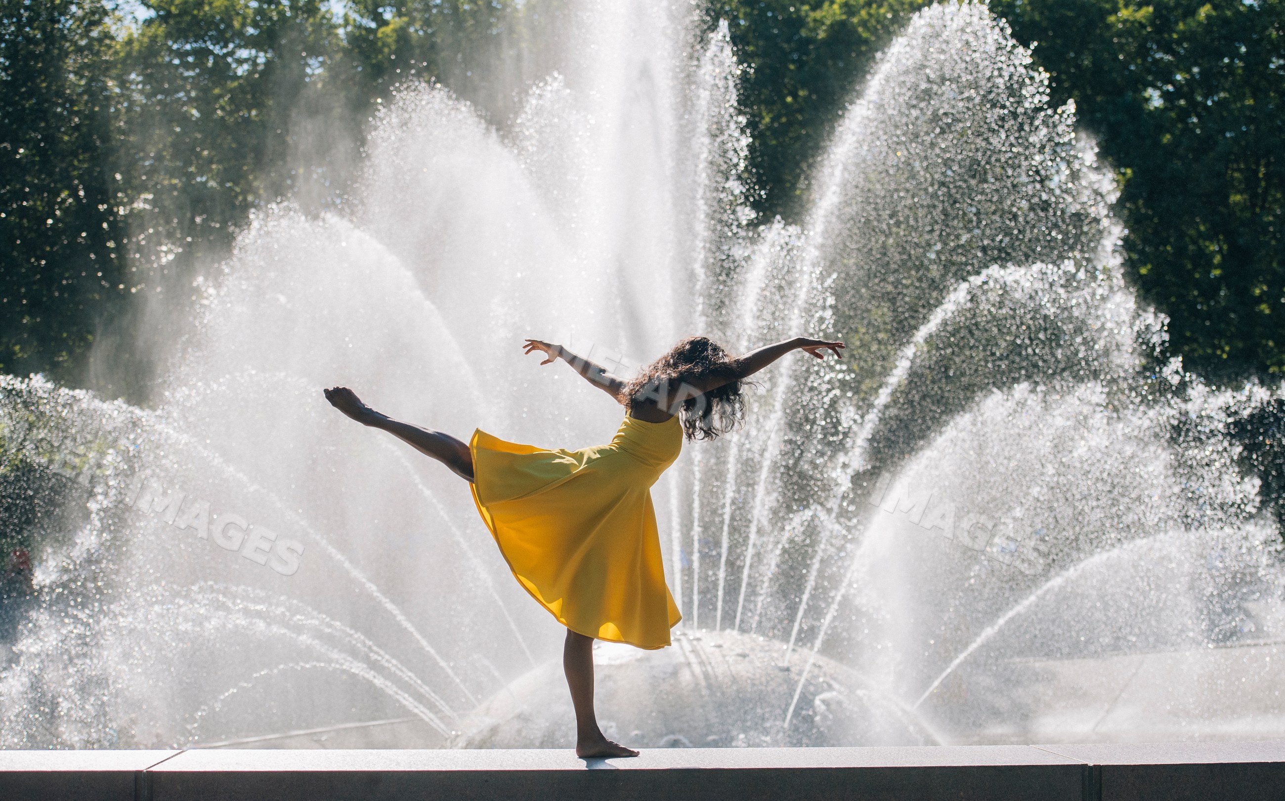 South Asian woman in yellow dress dancing ballet pose near fountain