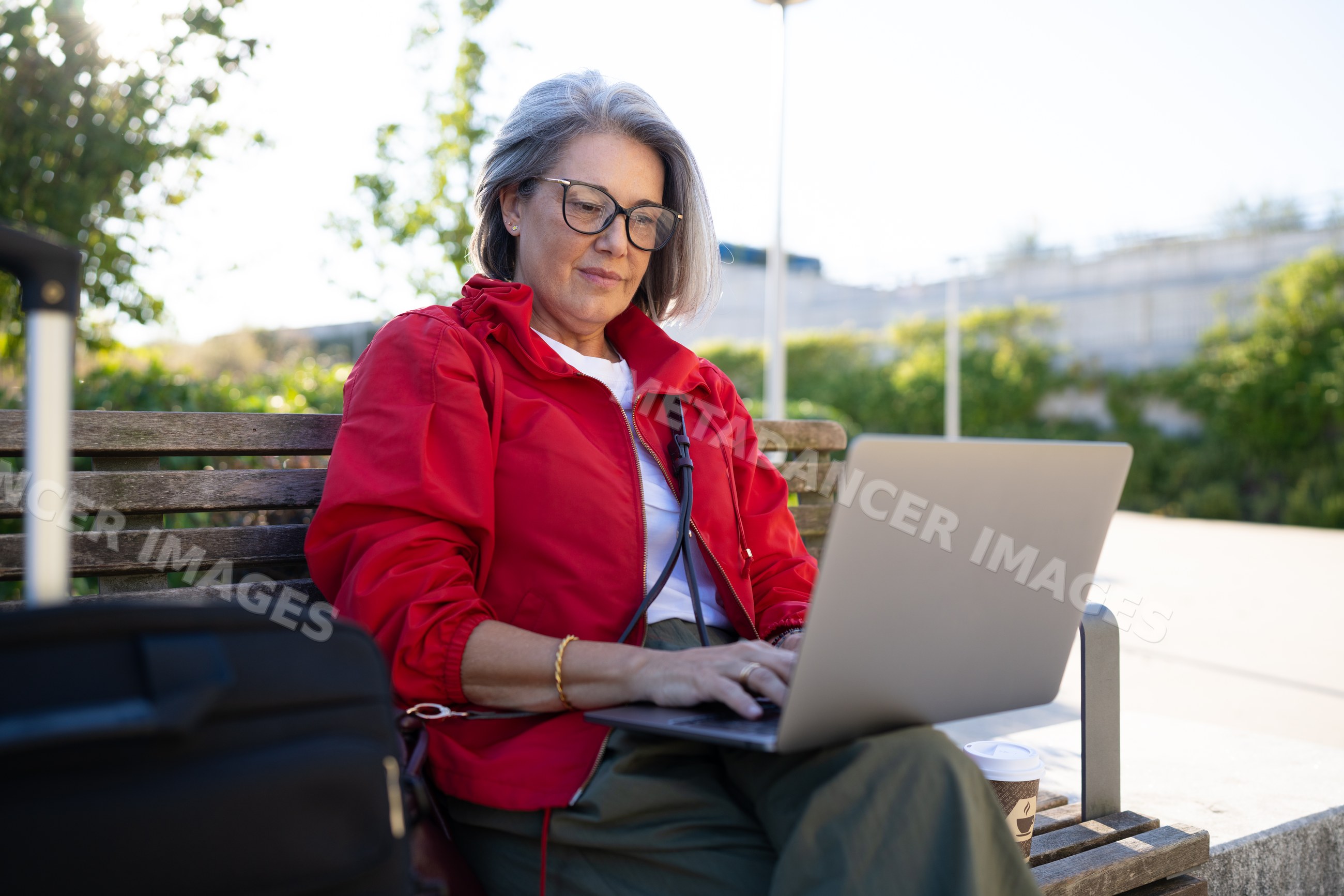 White woman working on laptop outdoors on a bench