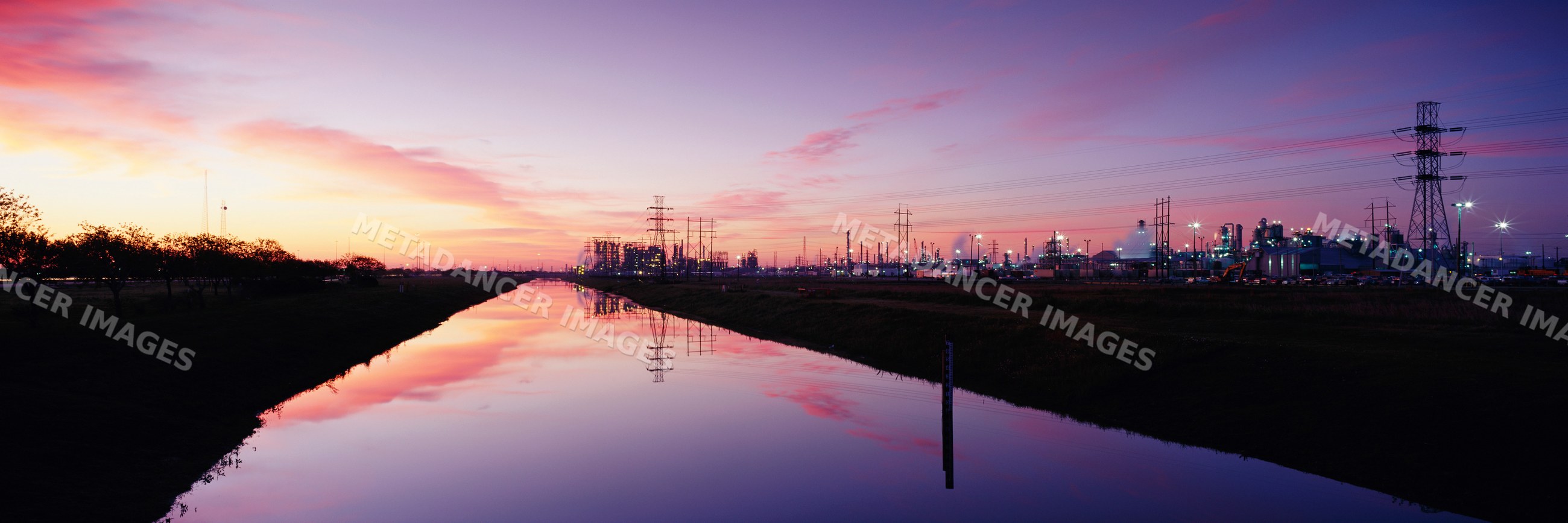 Oil refinery reflecting in canal at sunset
