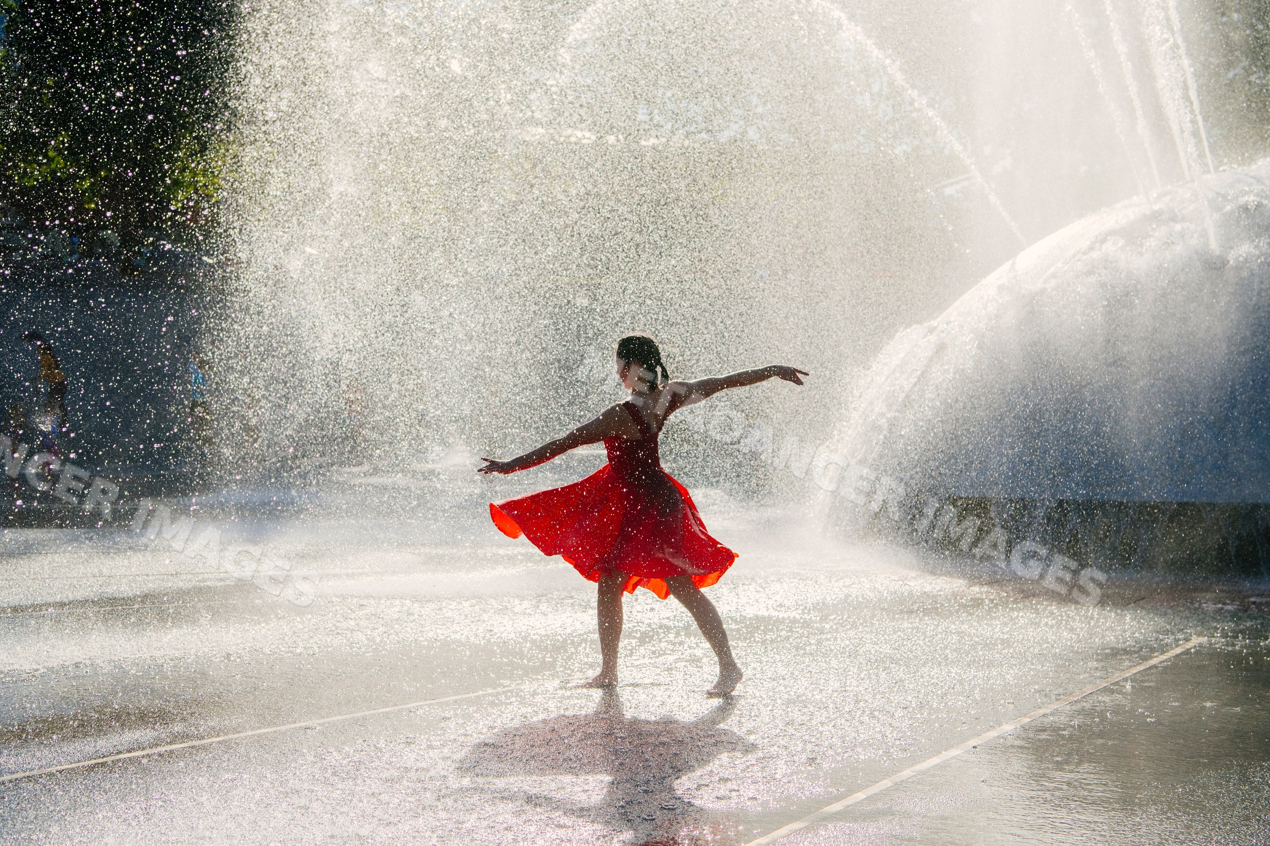 White girl dancing barefoot in red dress in water fountain outdoors