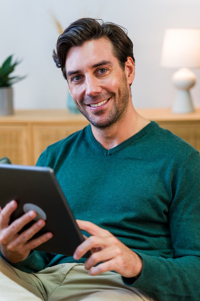 White man smiling while using a tablet in modern indoor living space