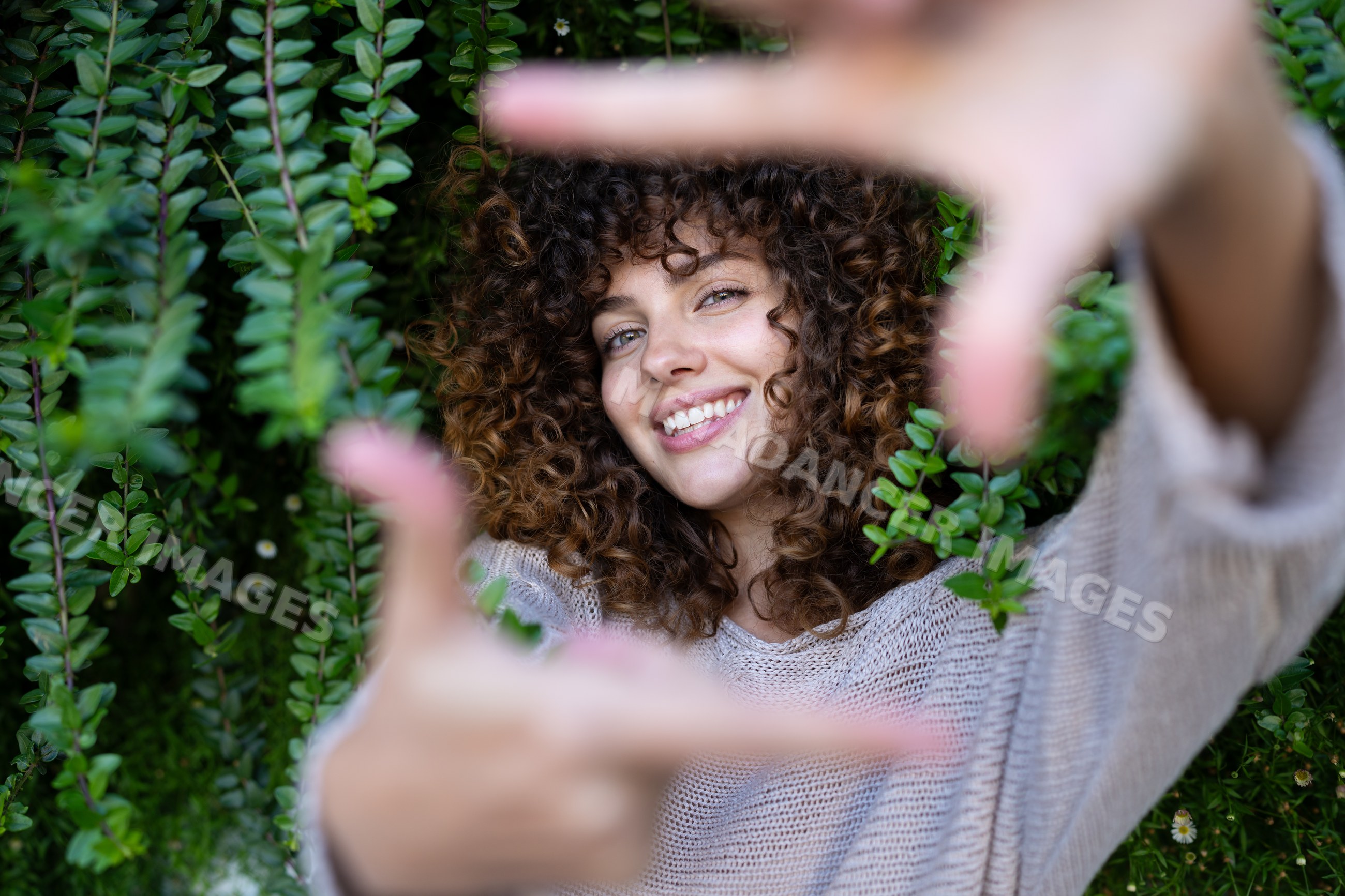 White woman framing face with hands outdoors in greenery in Spain
