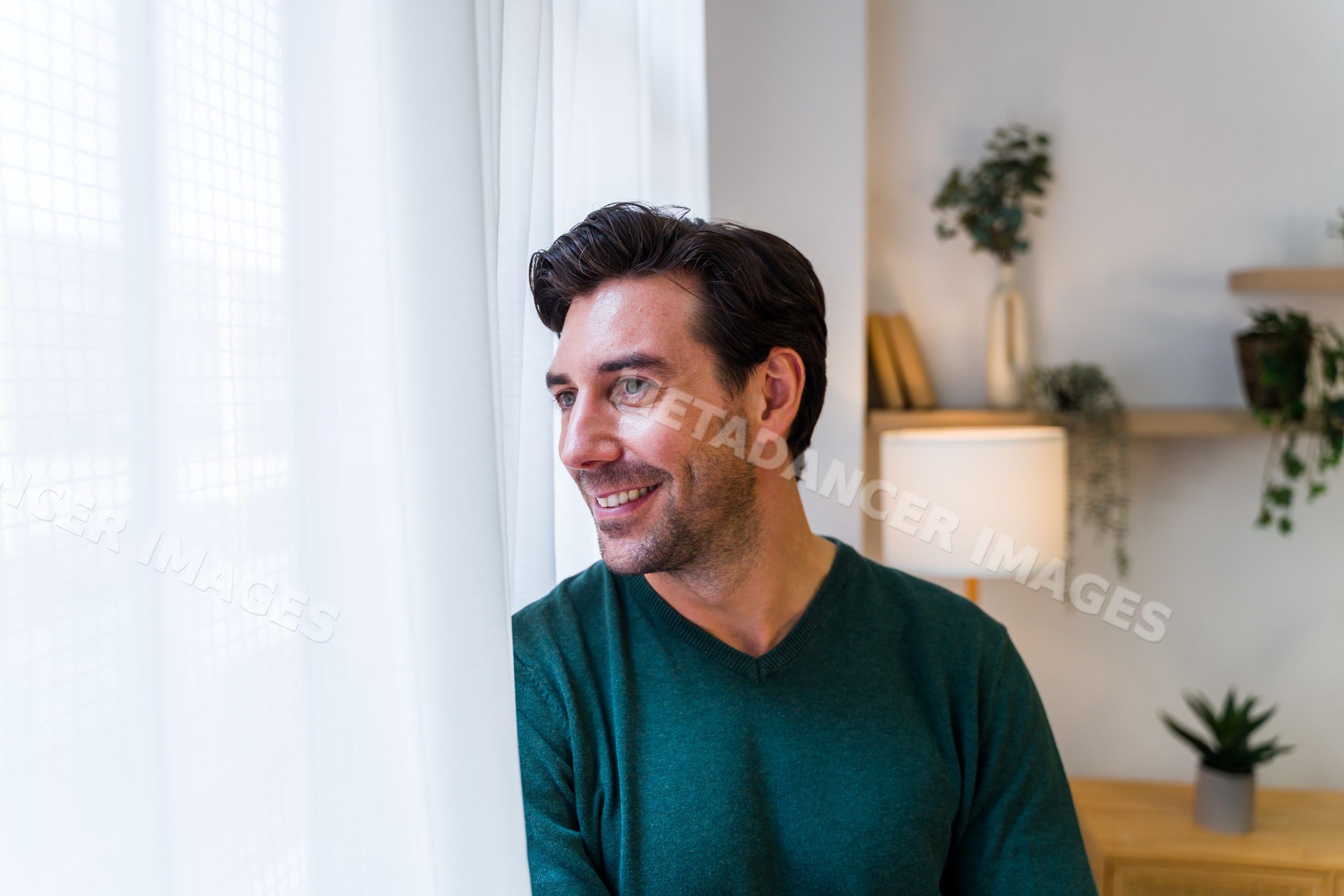 White man smiling while looking out window in modern living room