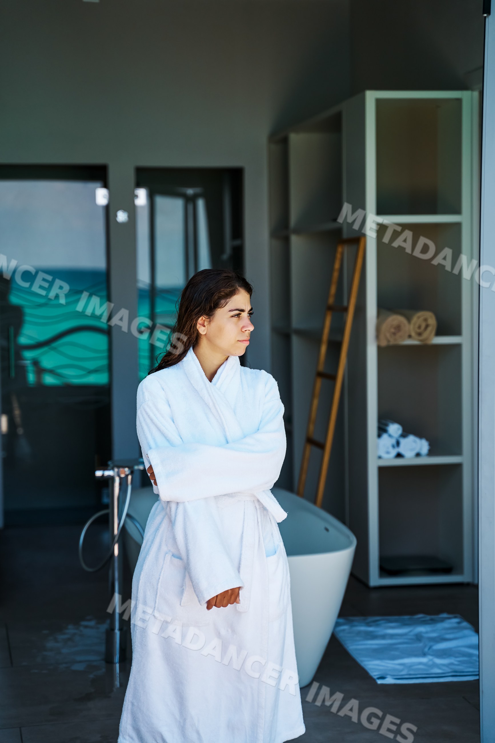 Woman in a white bathrobe stands inside a modern spa bathroom