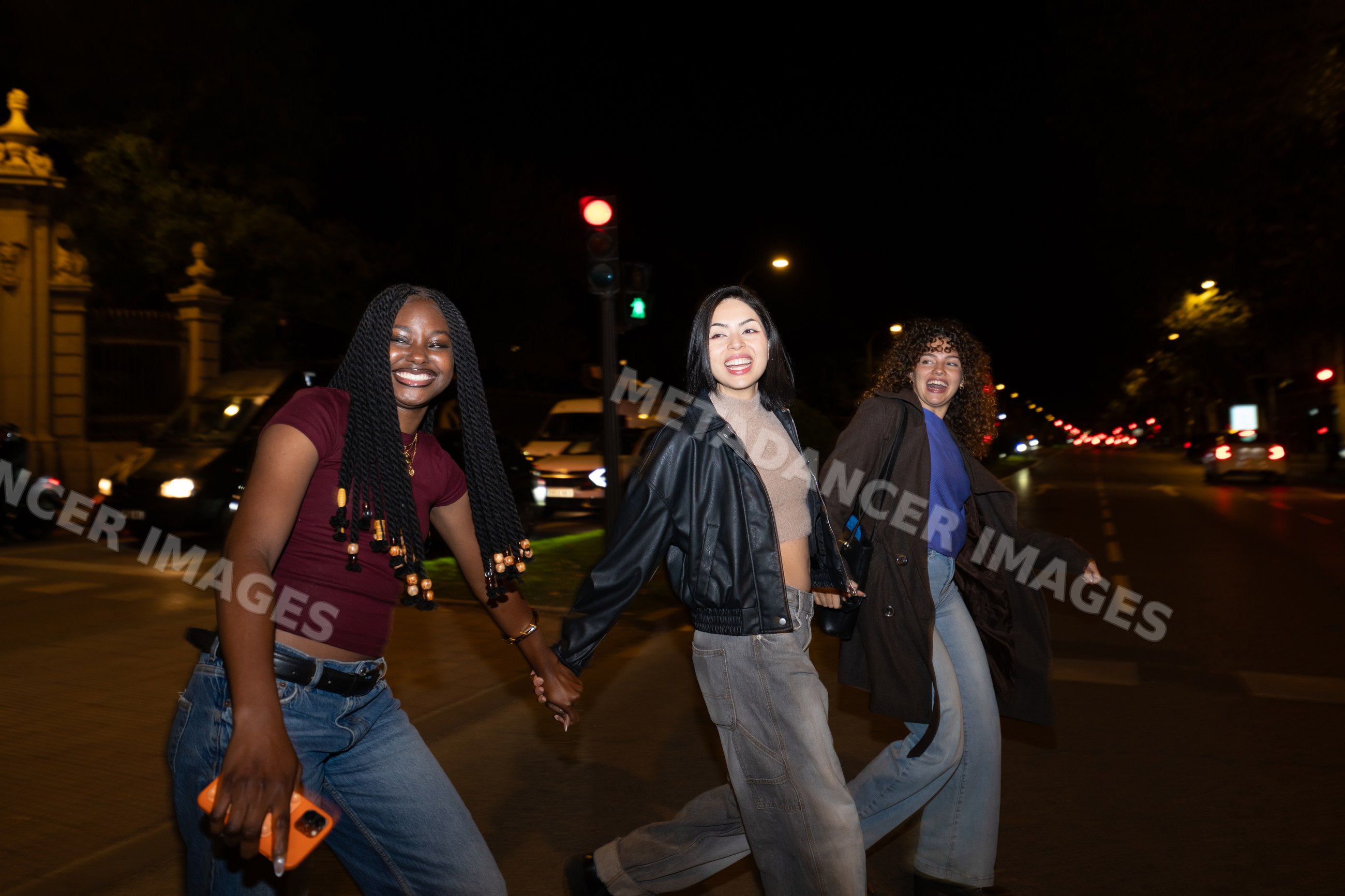 Three friends holding hands and walking across city street at night