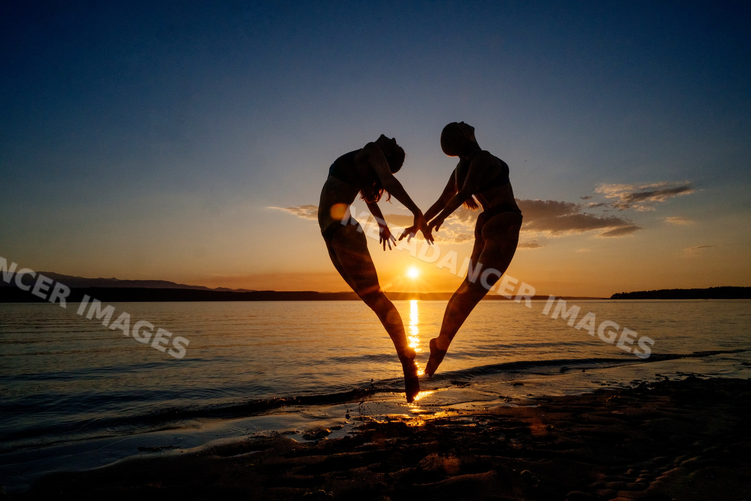 Two white people doing partner acrobatics jumps on a beach at sunset