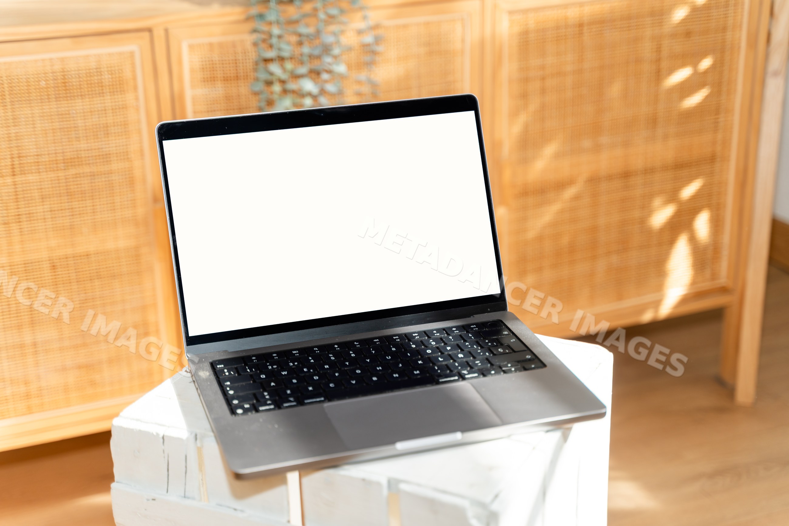 Laptop with blank white screen on wooden desk in sunlit interior