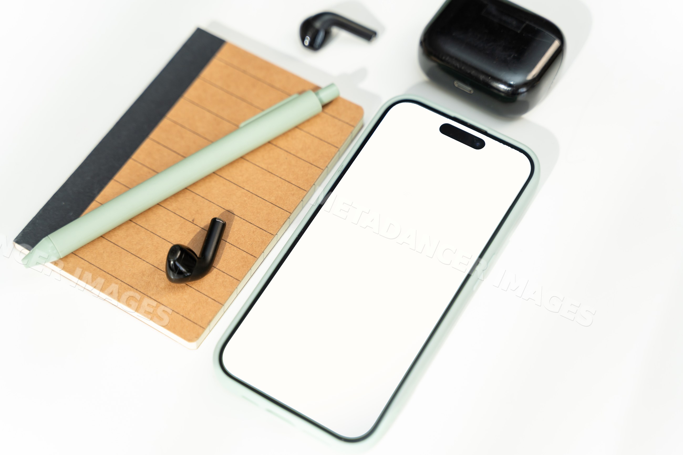 Smartphone with wireless earbuds, notebook, and pen on white surface