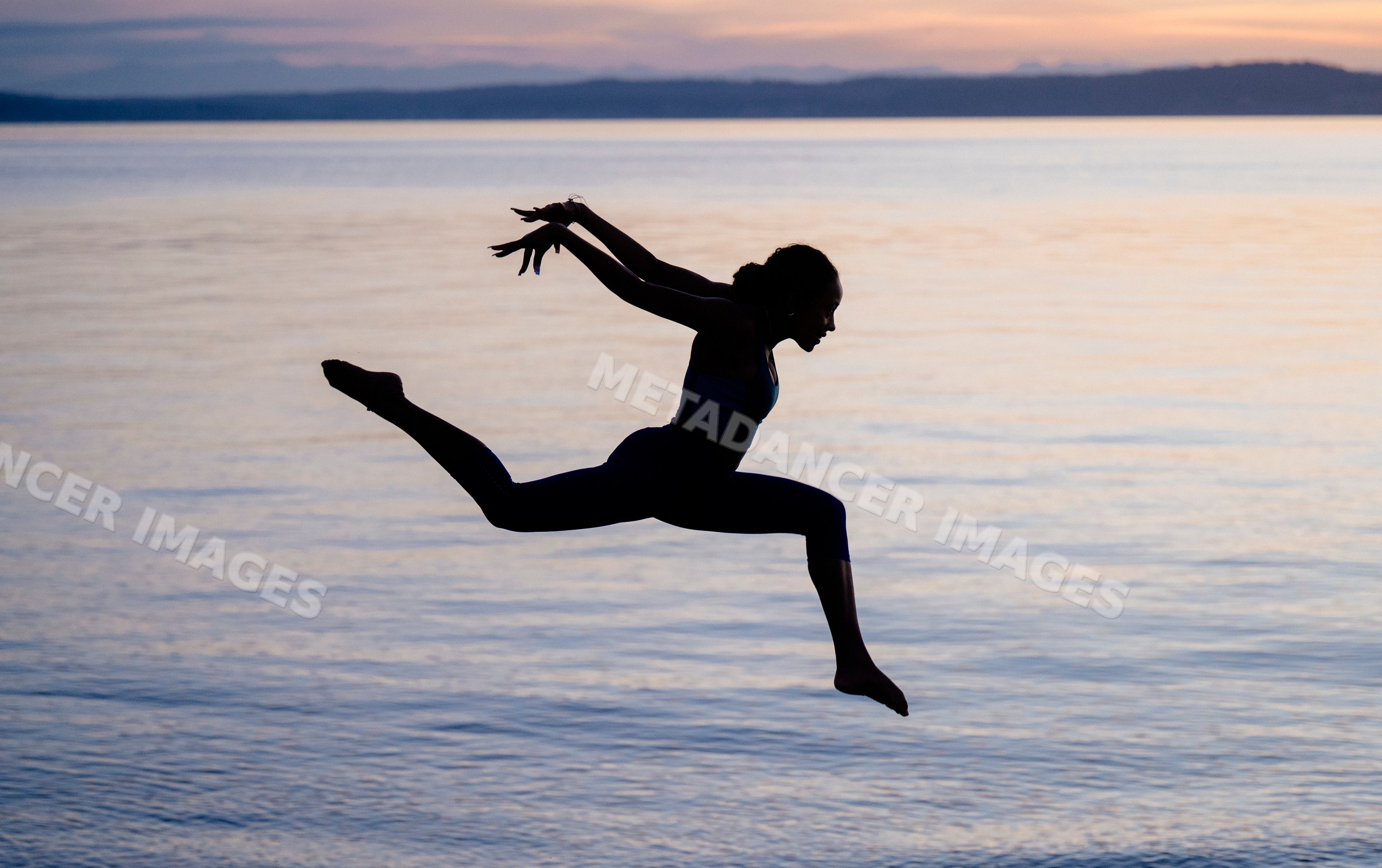 Hispanic woman performing an acrobatic yoga jump over lake water