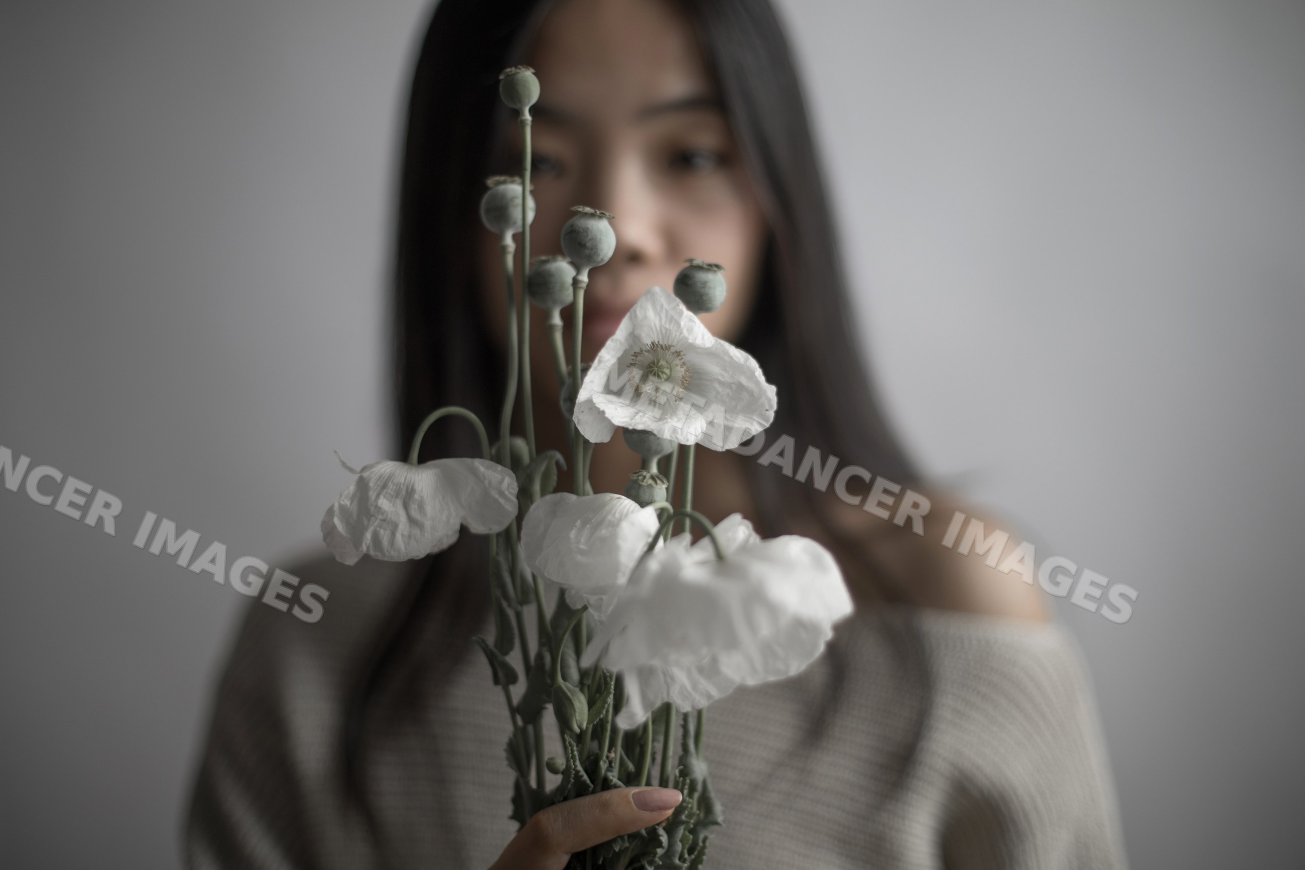Southeast Asian woman holding white poppy flowers with seed pods