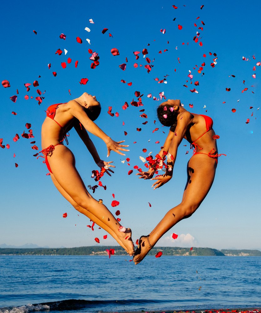 Two women jump gracefully with flower petals on a beach in WA, USA