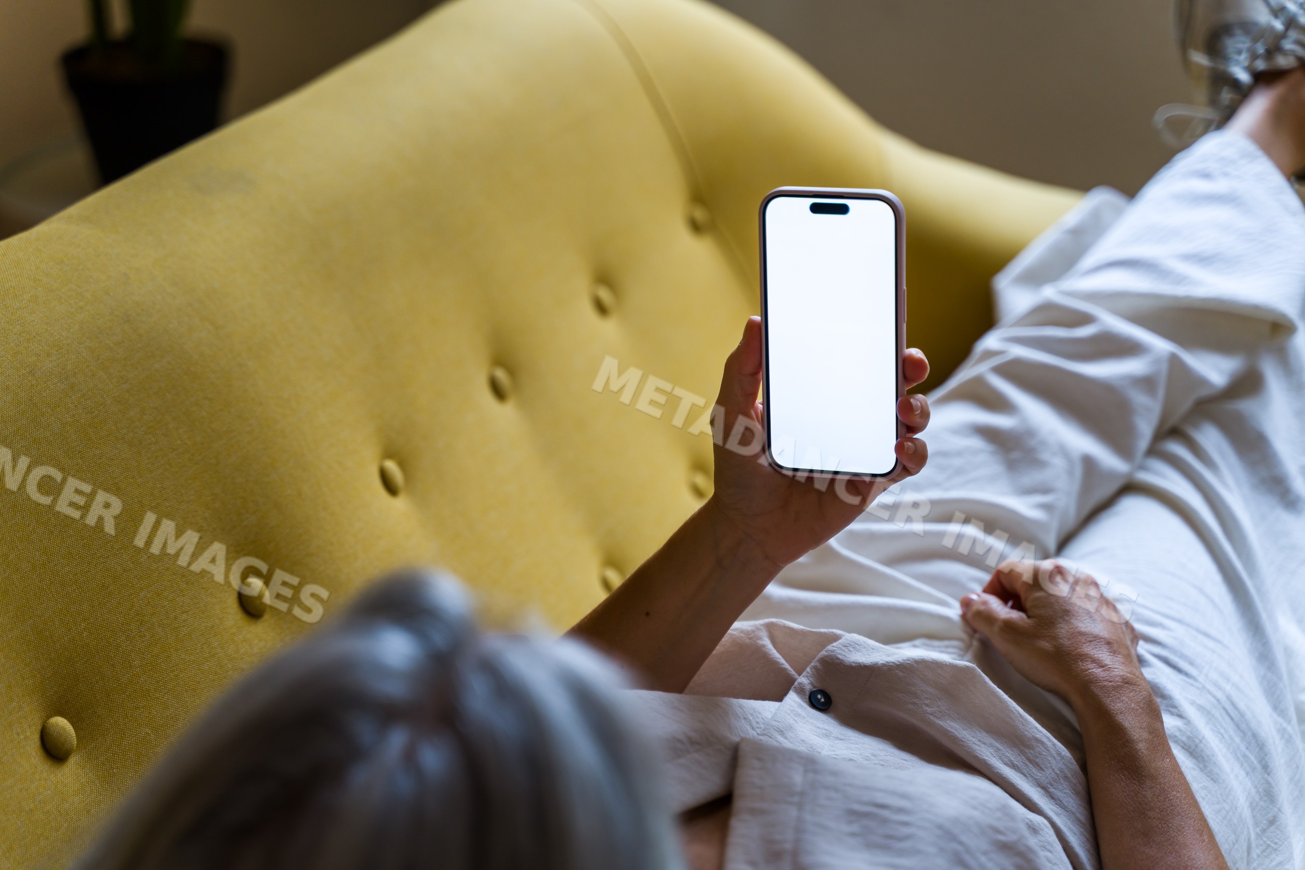 White person holding smartphone with blank screen on yellow sofa