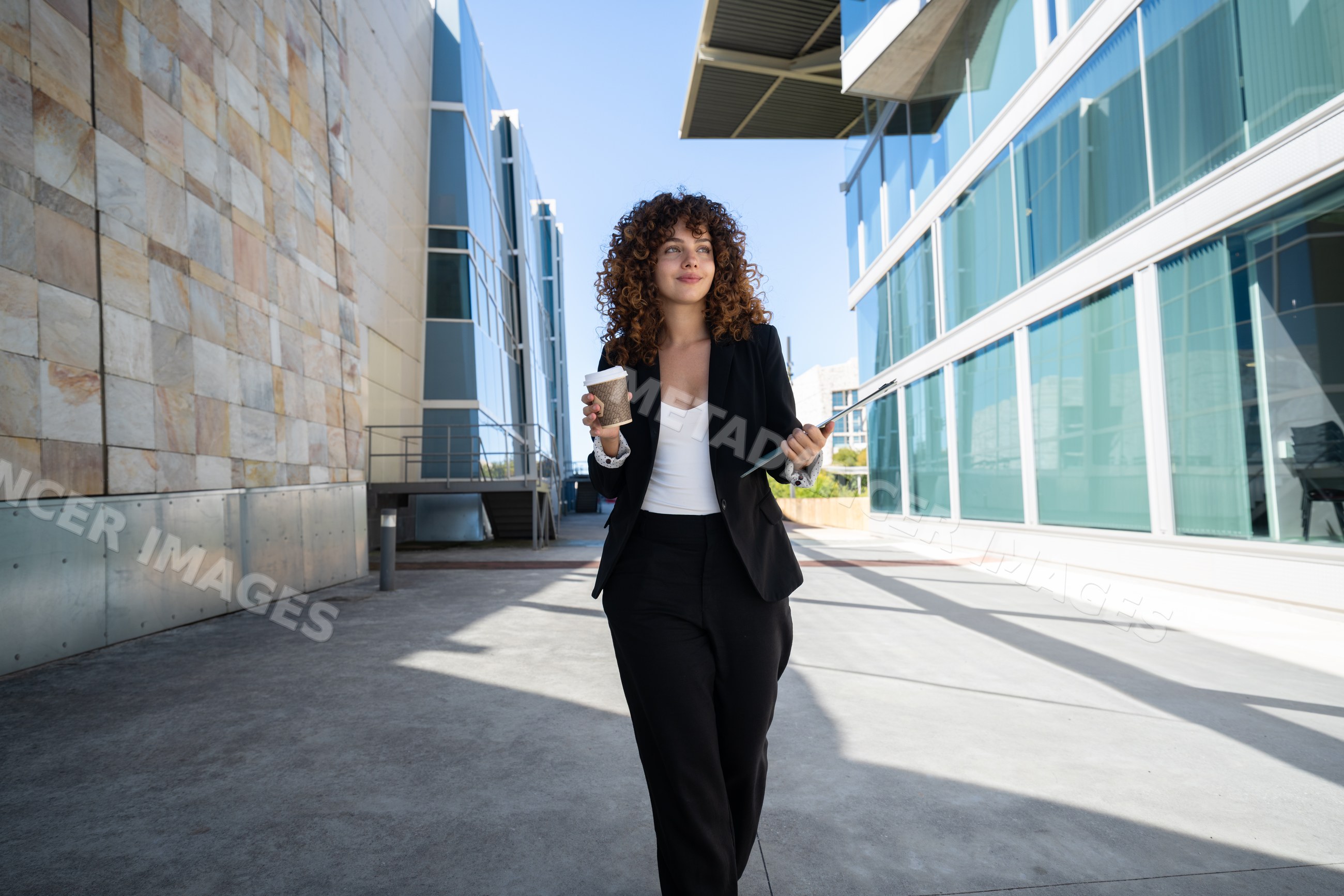 Businesswoman walking outdoors with coffee and folder in office area