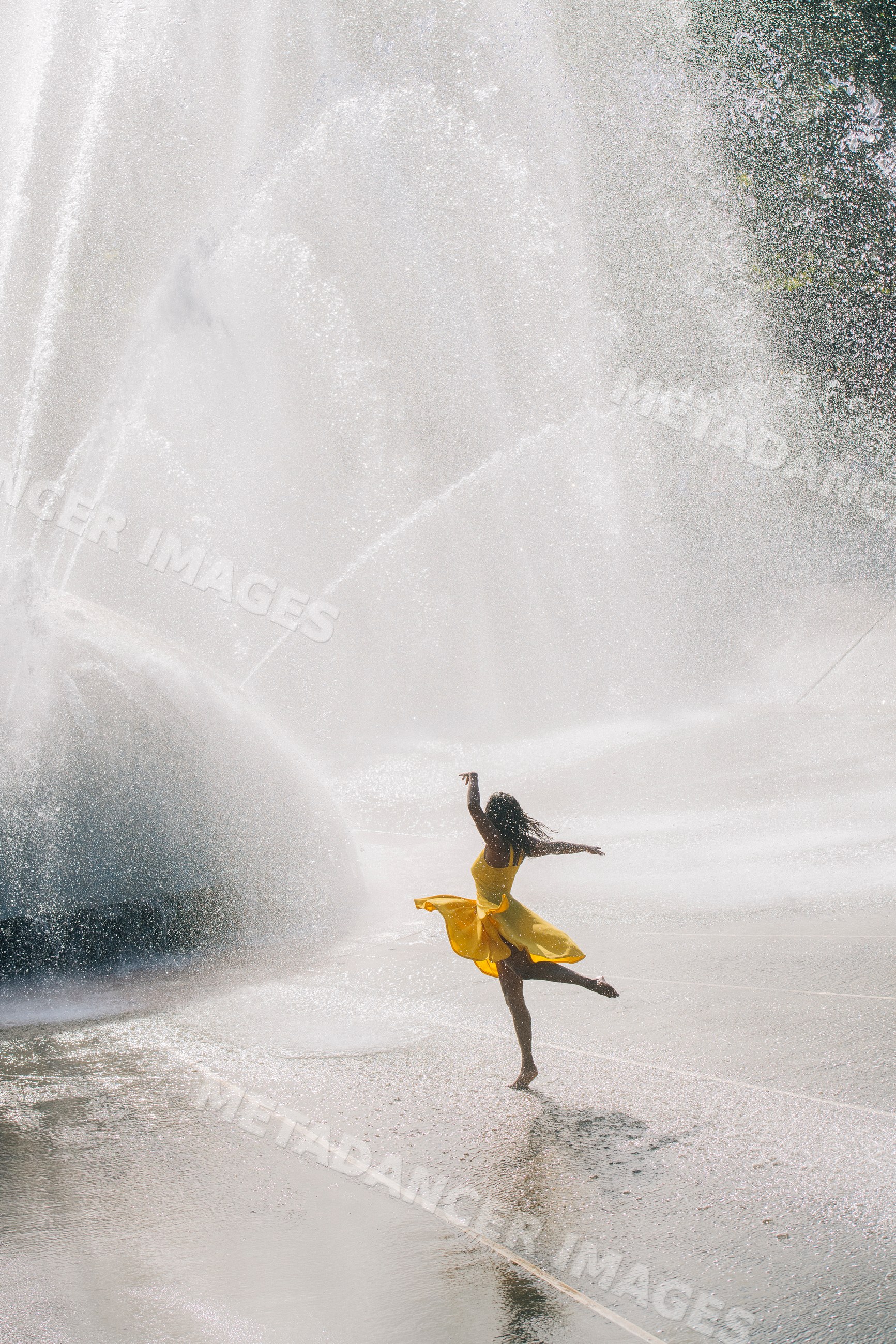 South Asian woman dancing in yellow dress at outdoor water fountain
