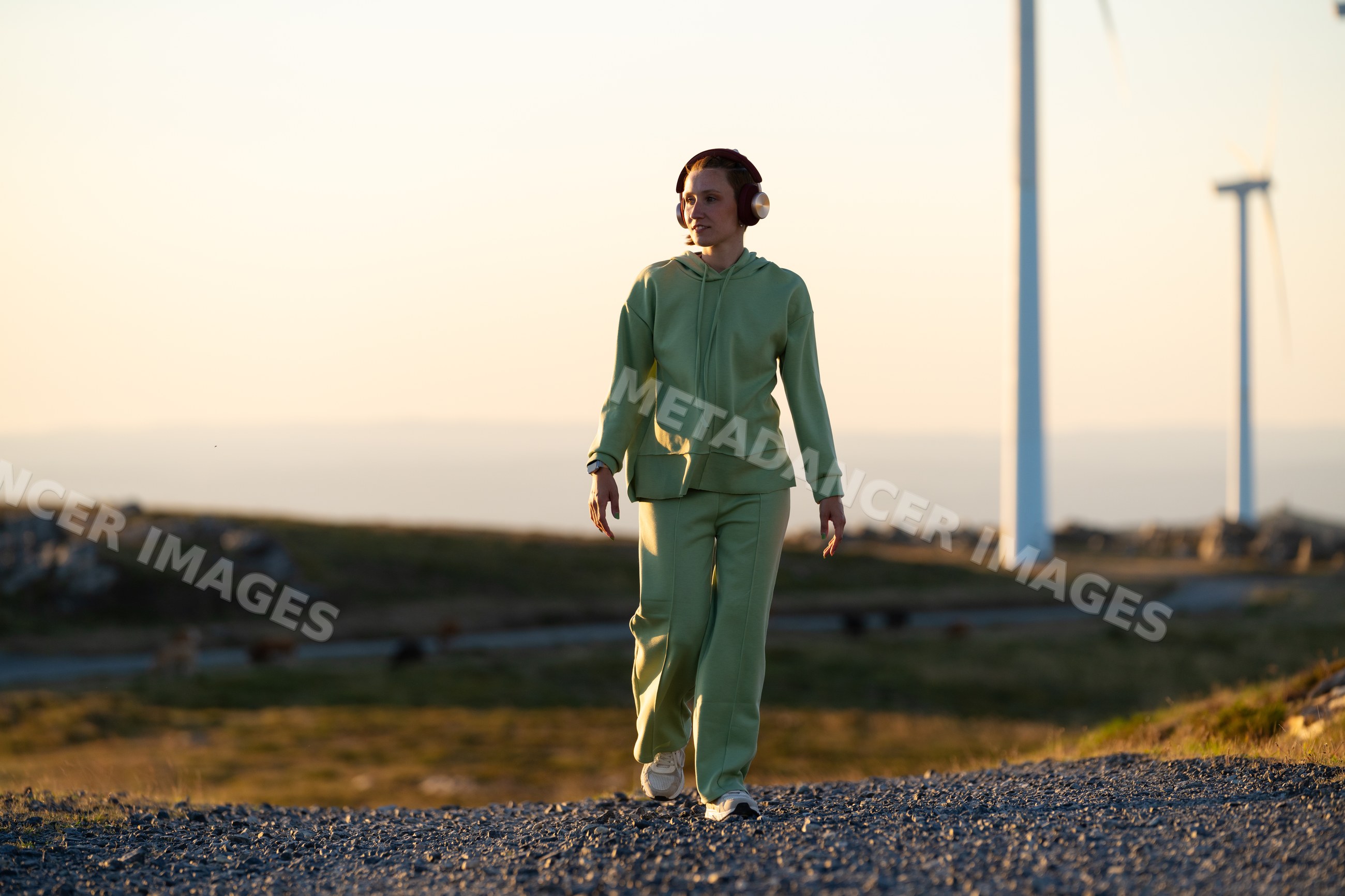 A white woman walks near wind turbines at sunset in Galicia, Spain