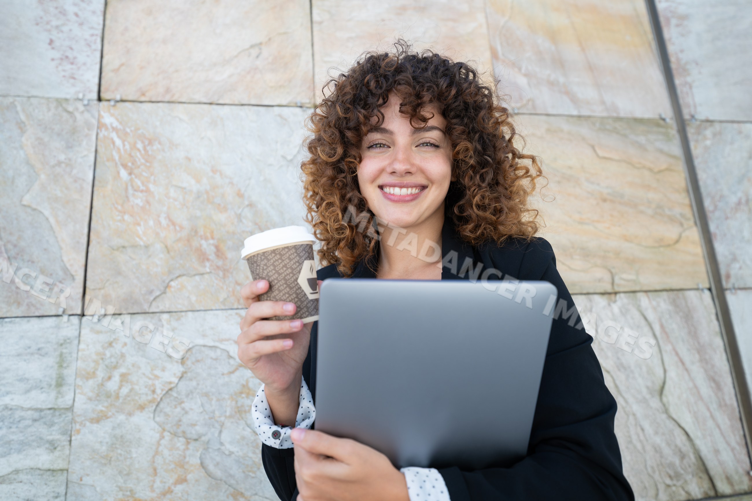 White woman holding laptop and coffee cup outdoors