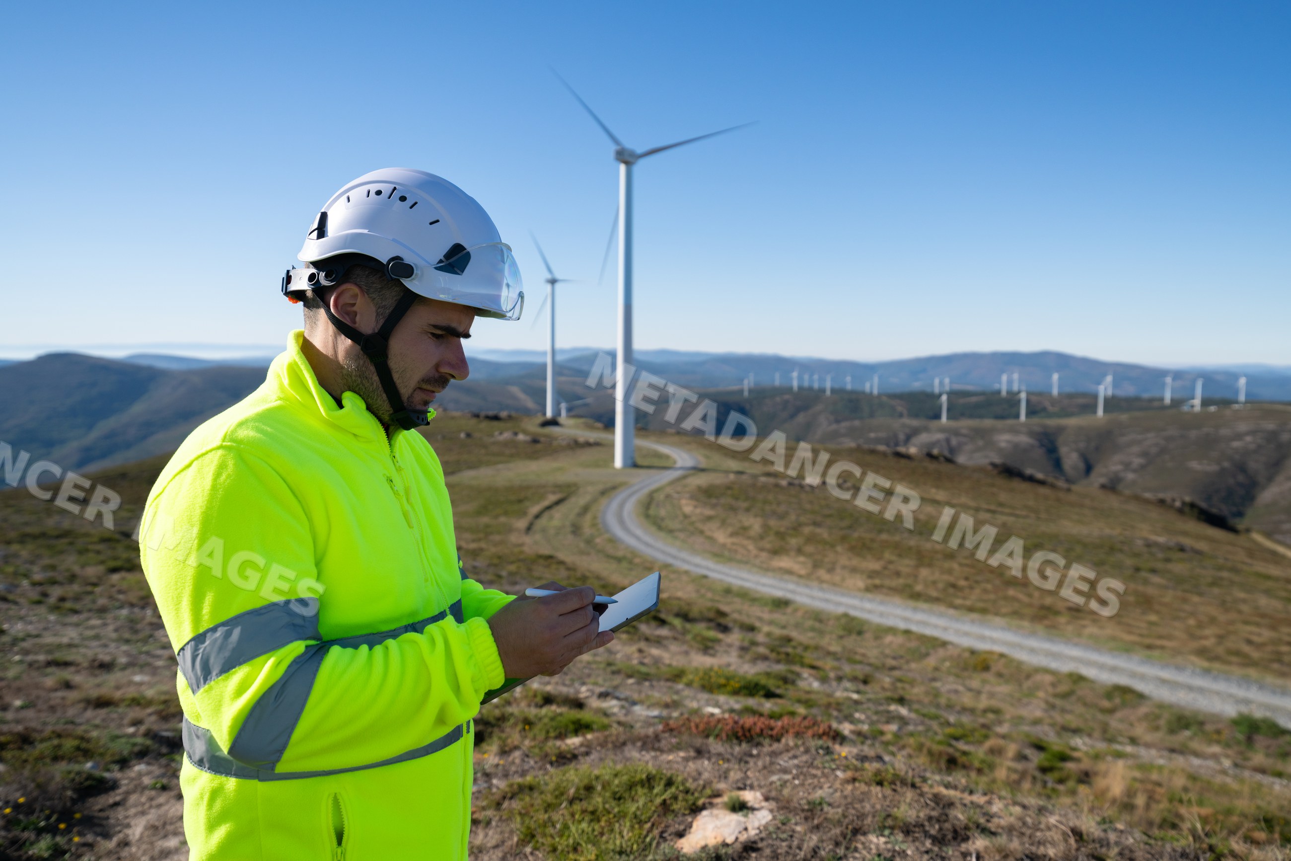 White worker with safety helmet using tablet at wind farm in Galicia