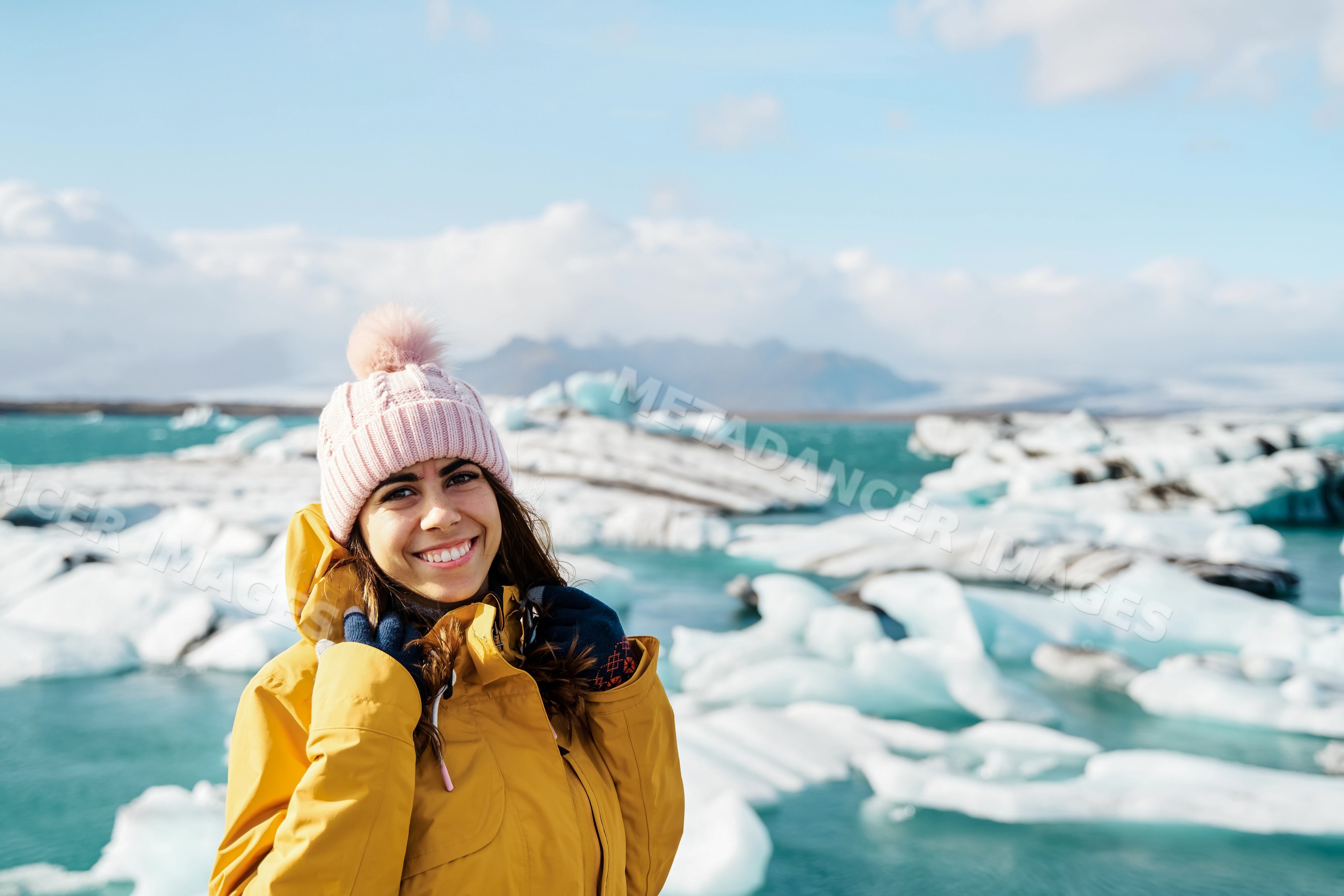 A smiling white woman in winter clothing stands by icebergs