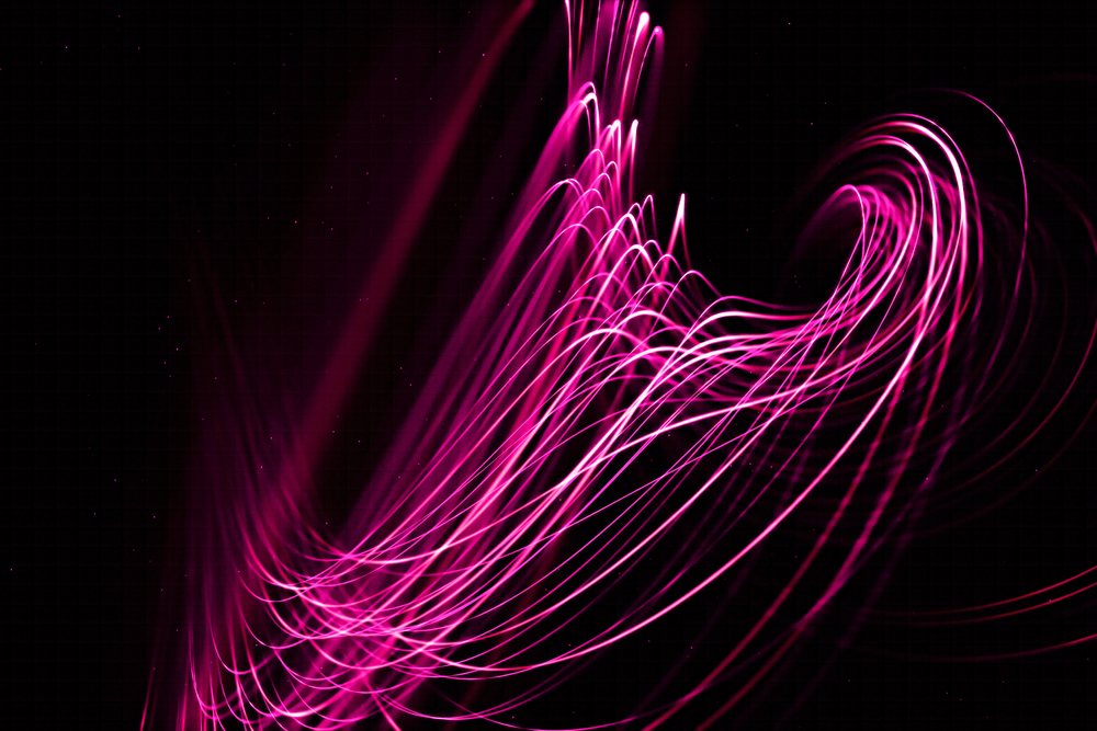 Pink light trails create abstract flowing patterns on a dark