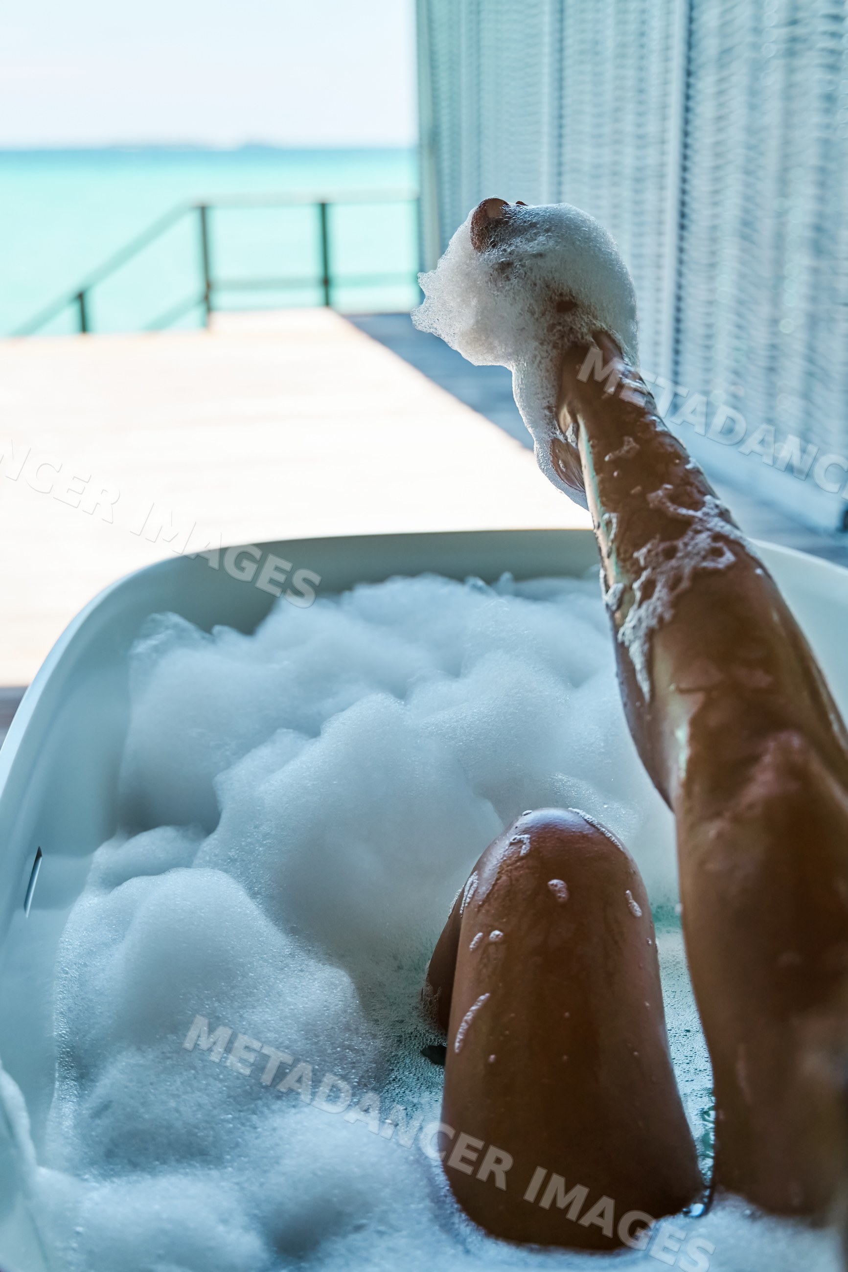 A white person enjoys a relaxing bubble bath with ocean view