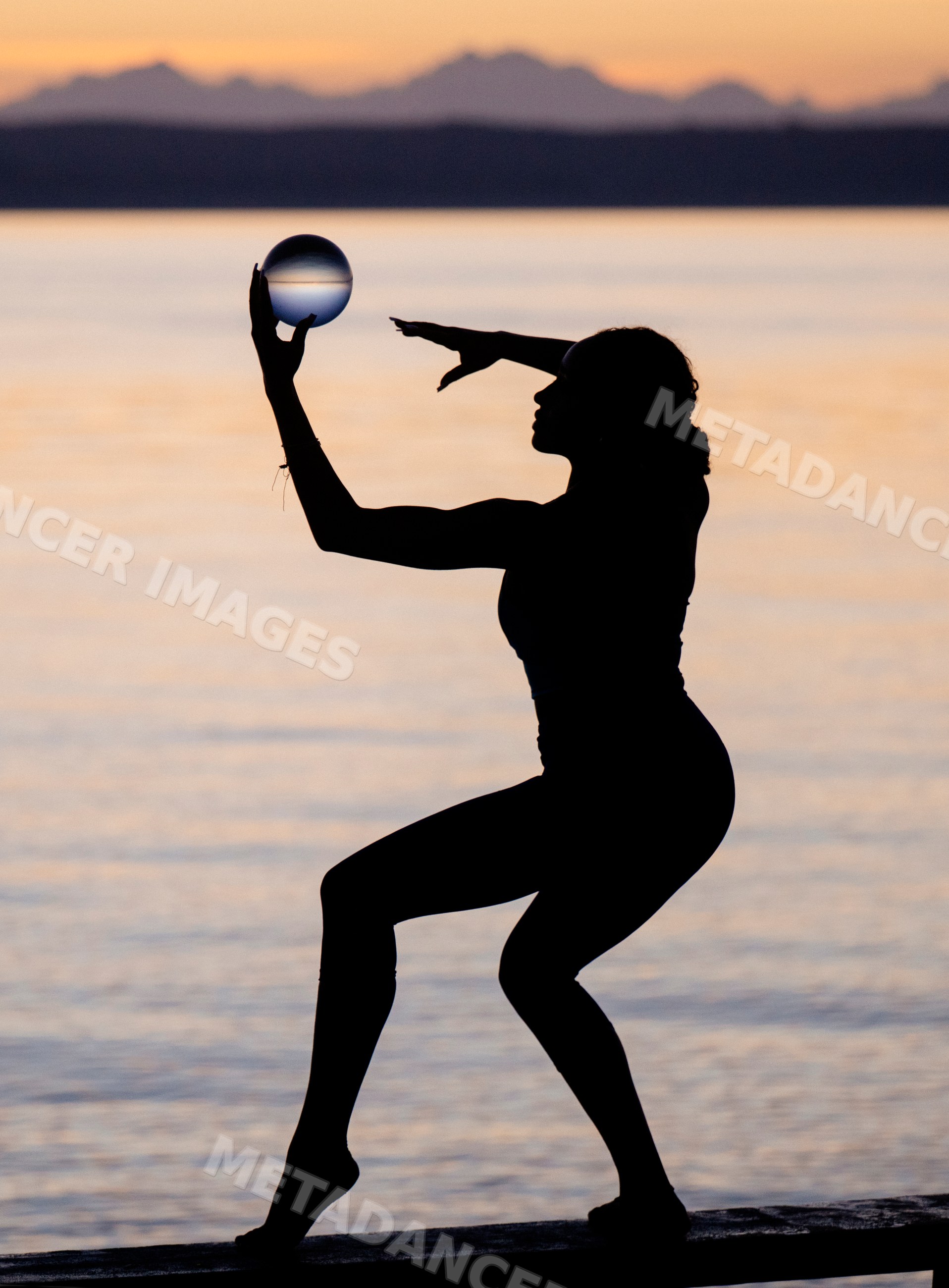 Silhouette of Hispanic woman doing acrobatic yoga pose with glass ball