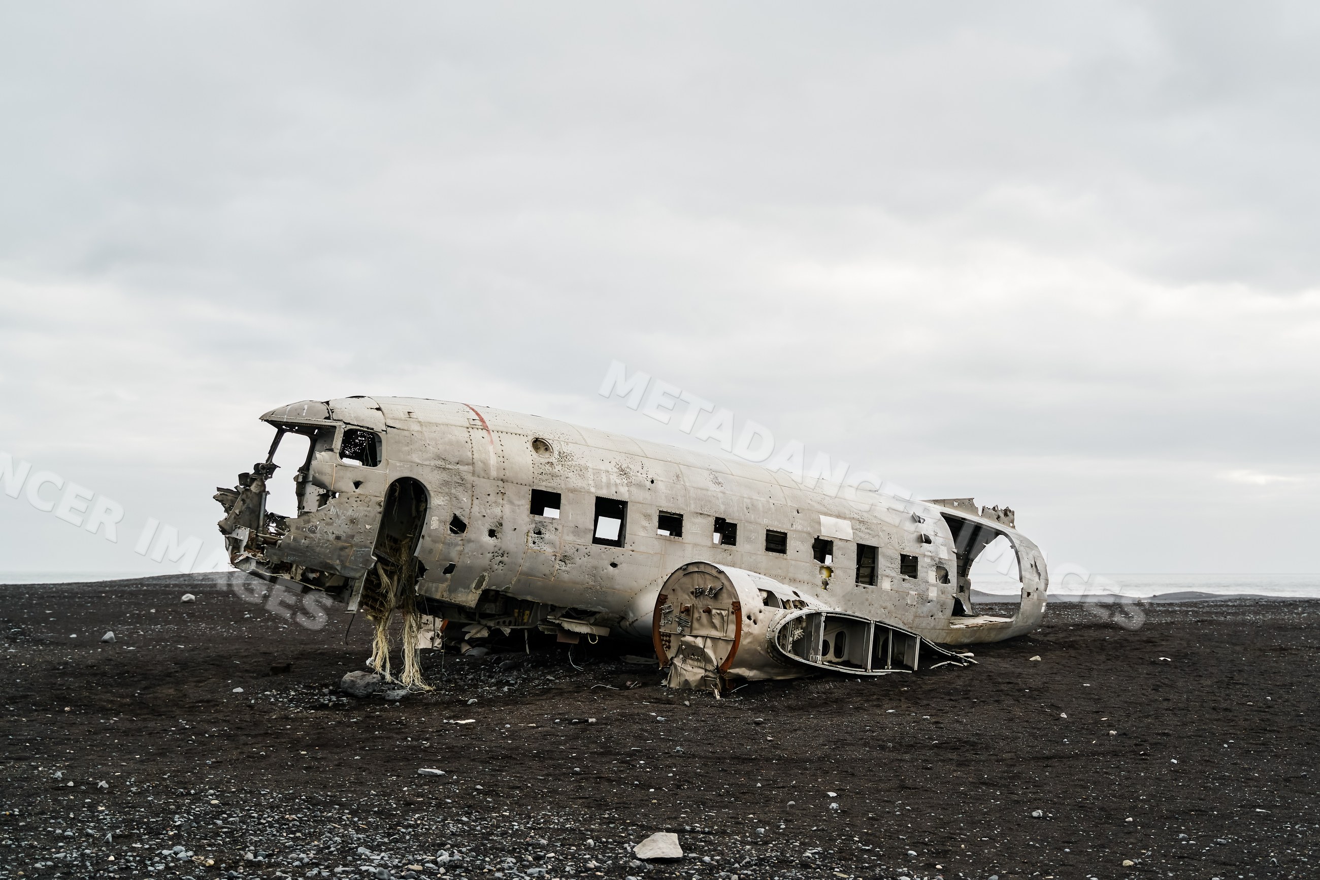 Old airplane wreckage lies on a black sand beach in a beach