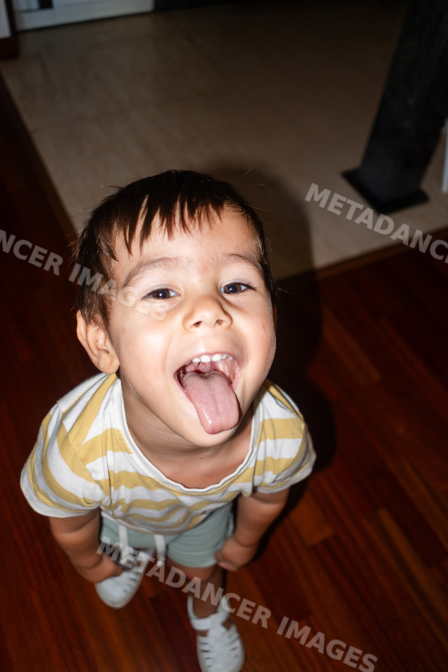 A young white boy playfully sticks out his tongue indoors on wood