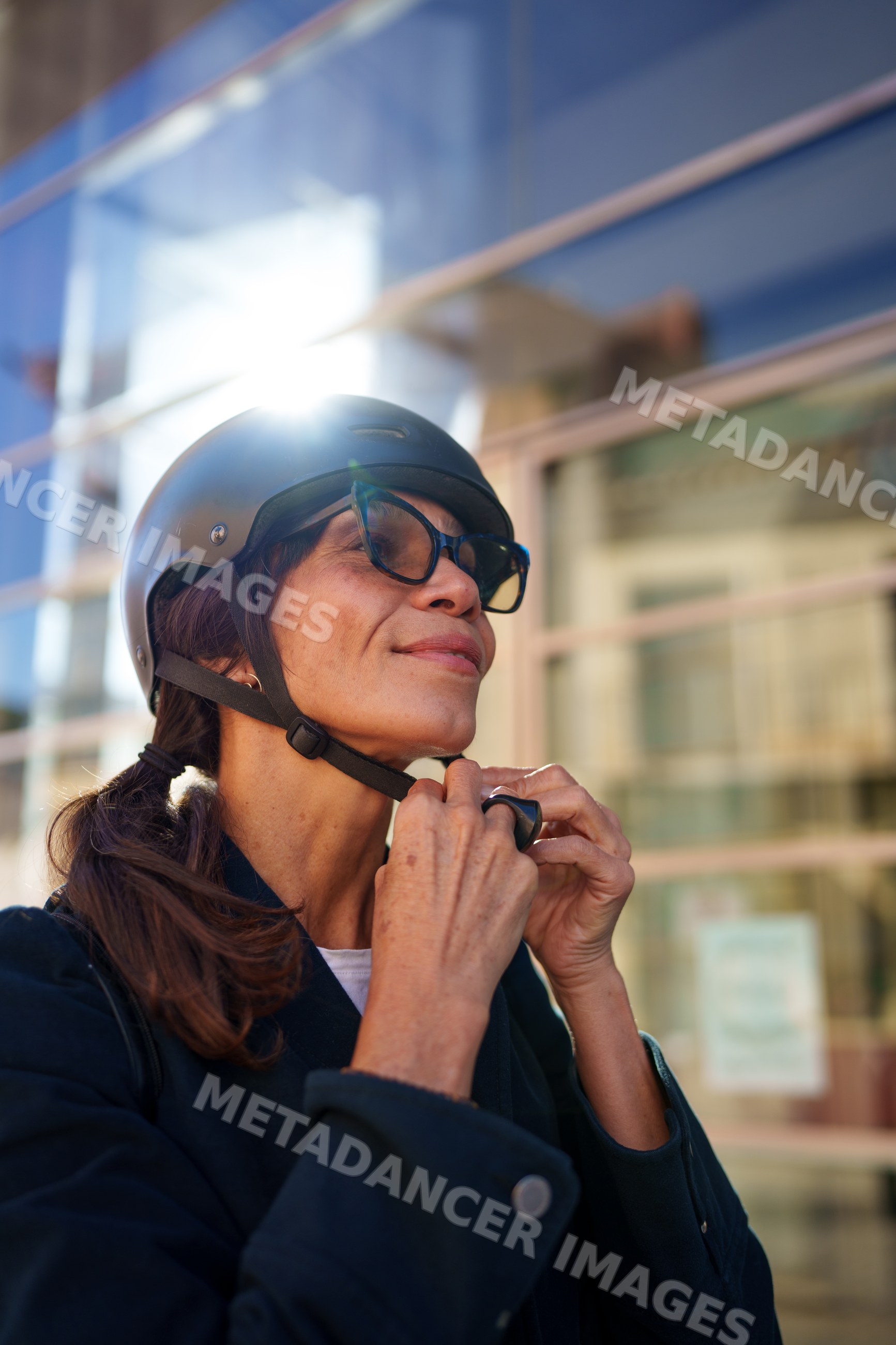 Hispanic woman putting on helmet outdoors in urban setting