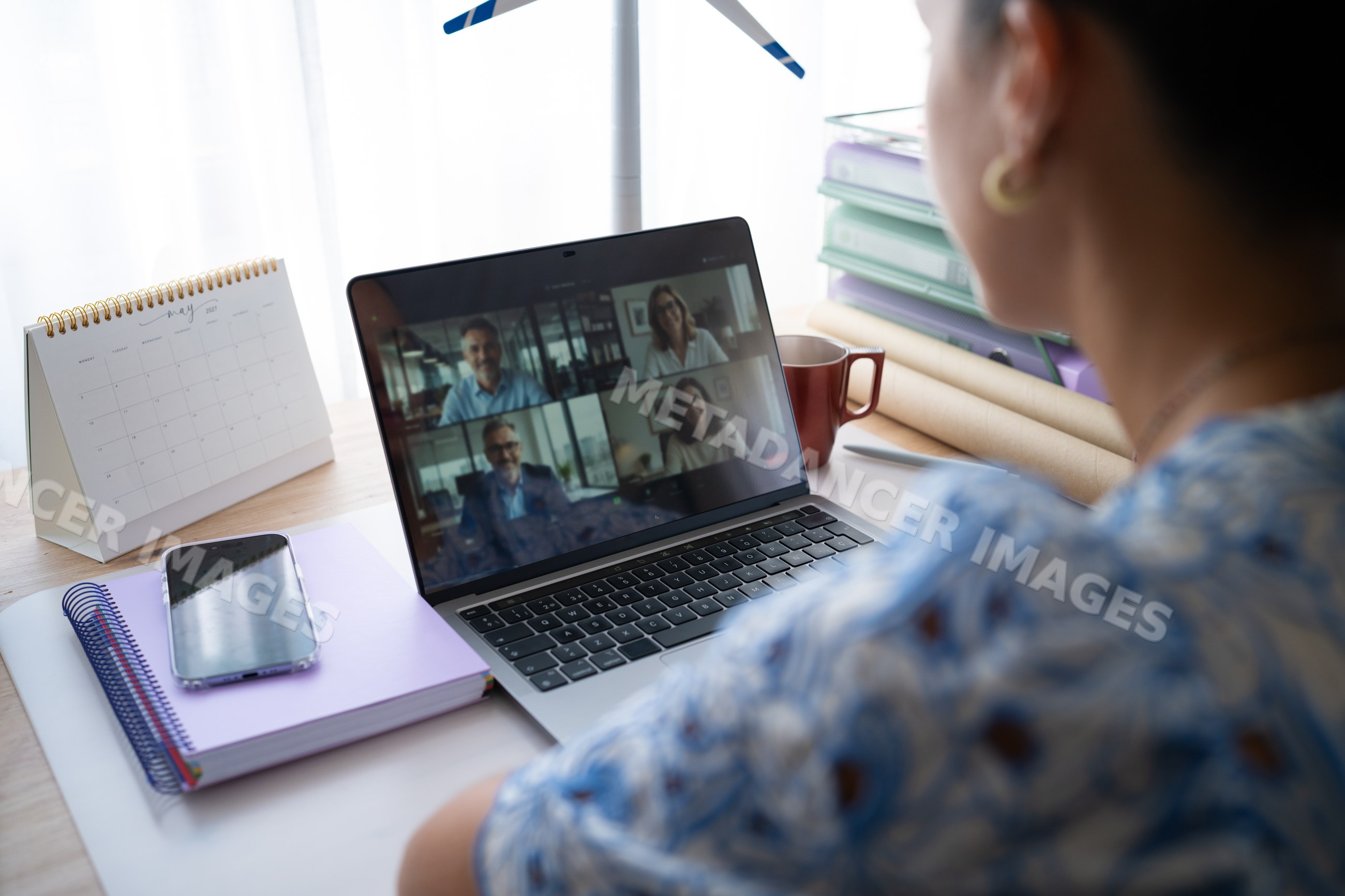 White woman on video call in home office with laptop and notebooks