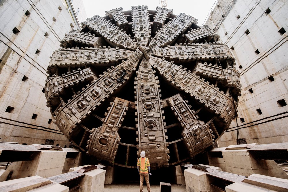 A white worker inspects a massive tunnel boring machine