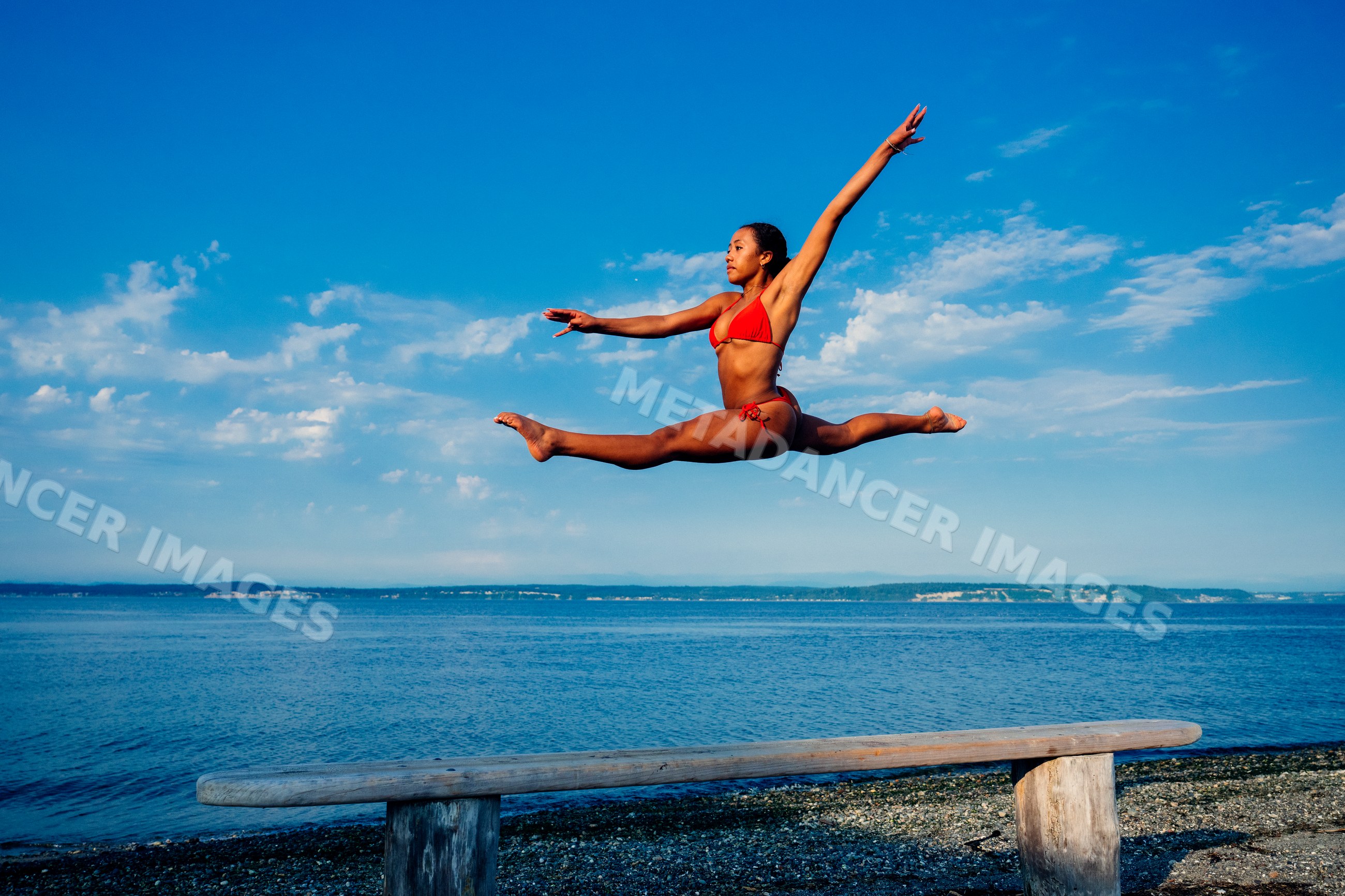 Woman jumping in a split over a bench on a beach in WA, USA