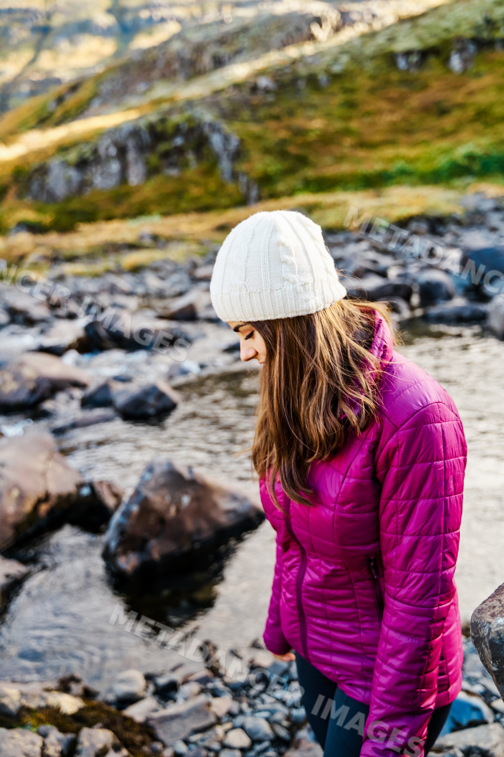 A white woman hikes near a rocky river in Iceland with warm outdoor