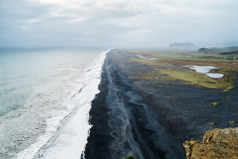 Aerial view of a black sand beach and ocean waves along an Iceland
