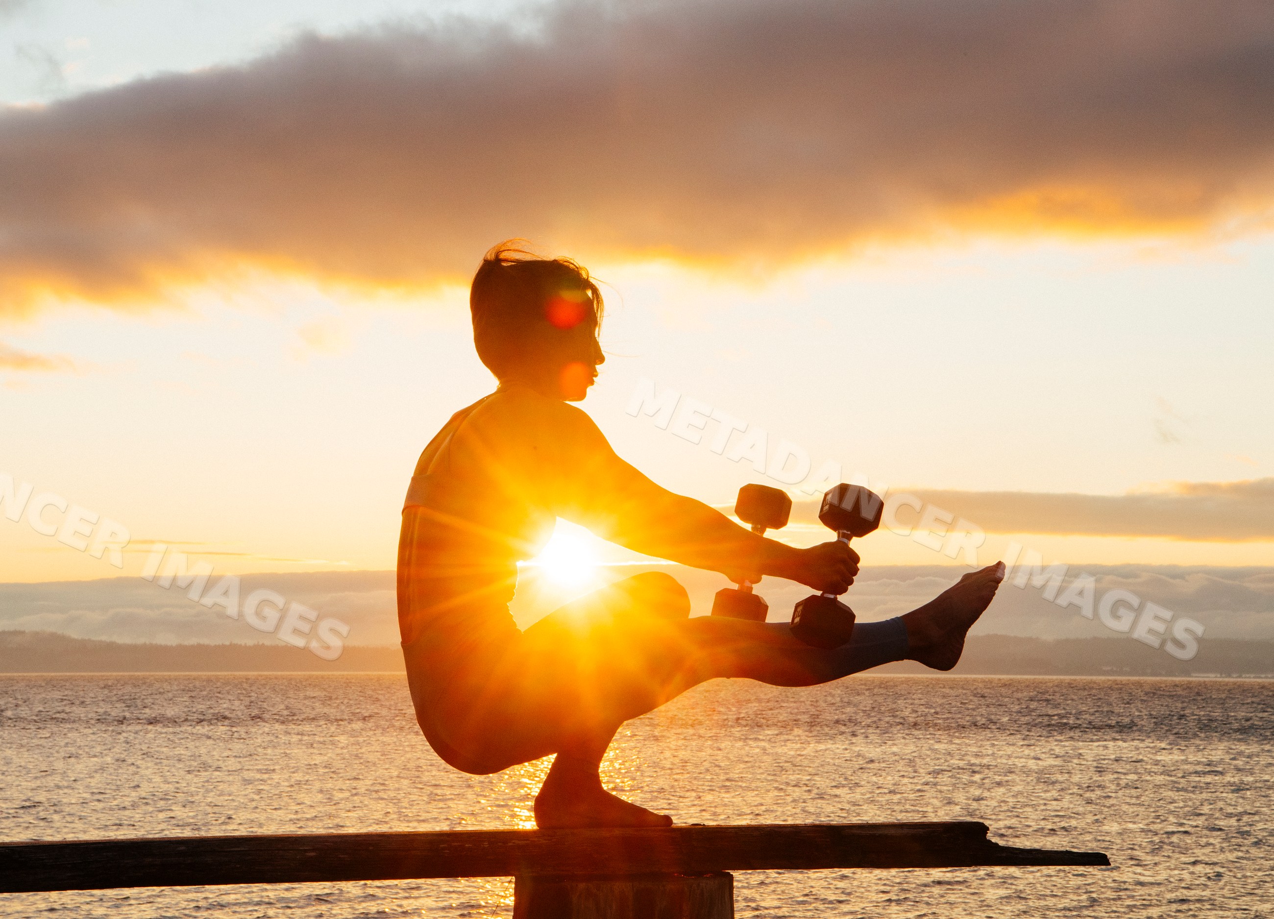 White woman exercising with dumbbells balancing outdoors at sunset