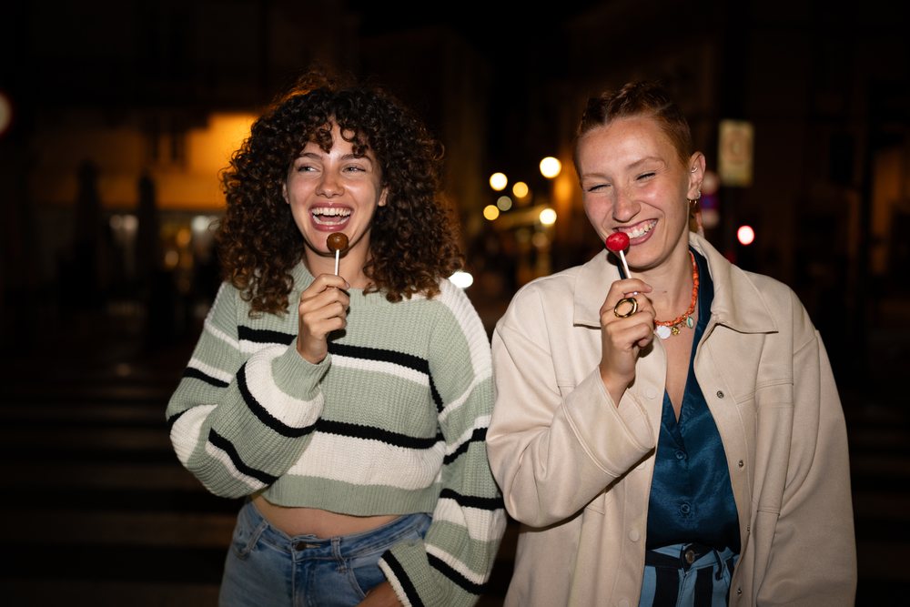 White women enjoying lollipops on a nighttime street in a street