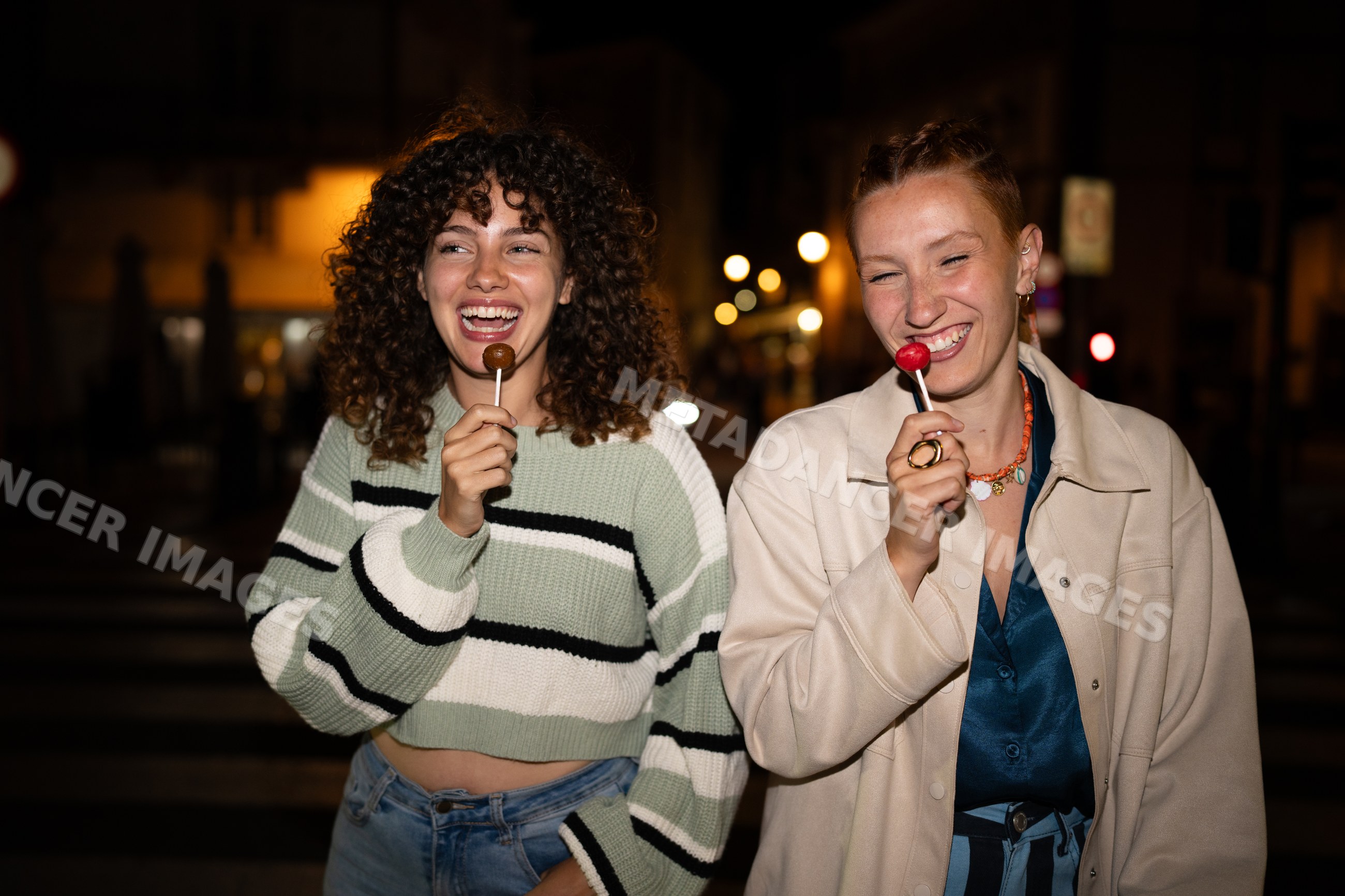 White women enjoying lollipops on a nighttime street in a street
