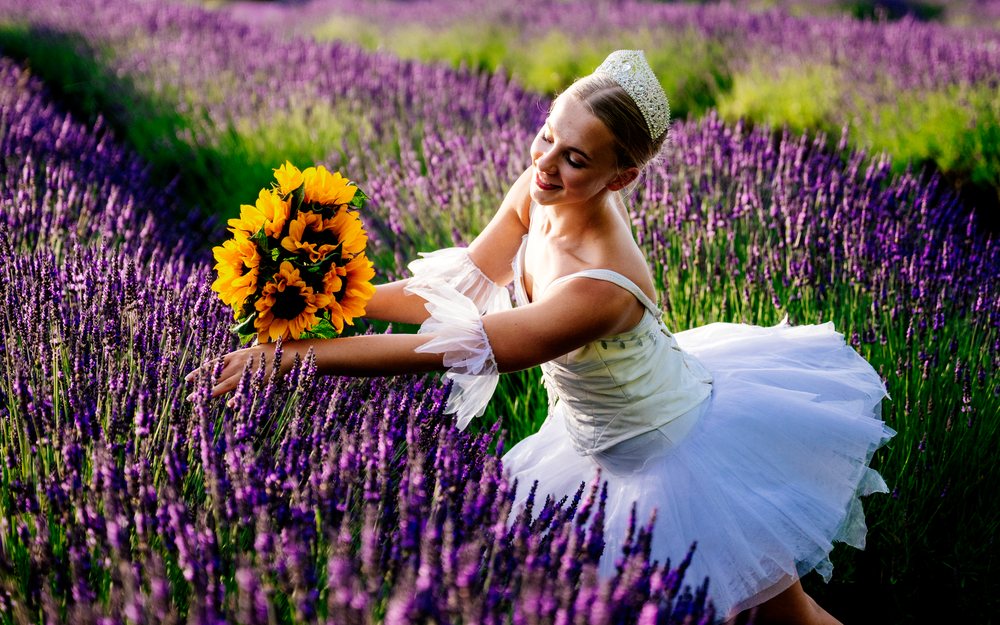A white dancer holds a sunflower bouquet in a lavender field