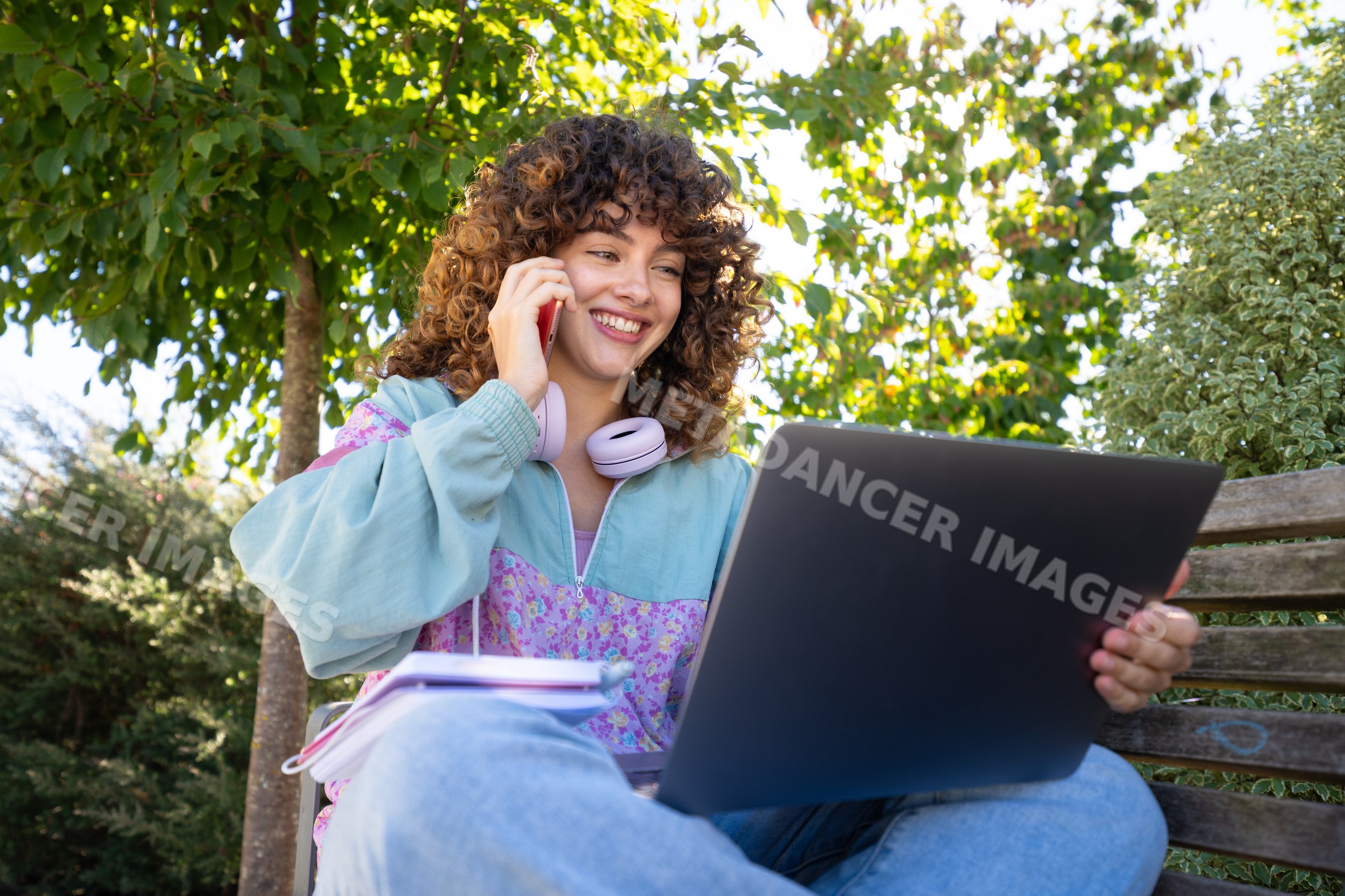 White woman using laptop and phone outdoors on park bench