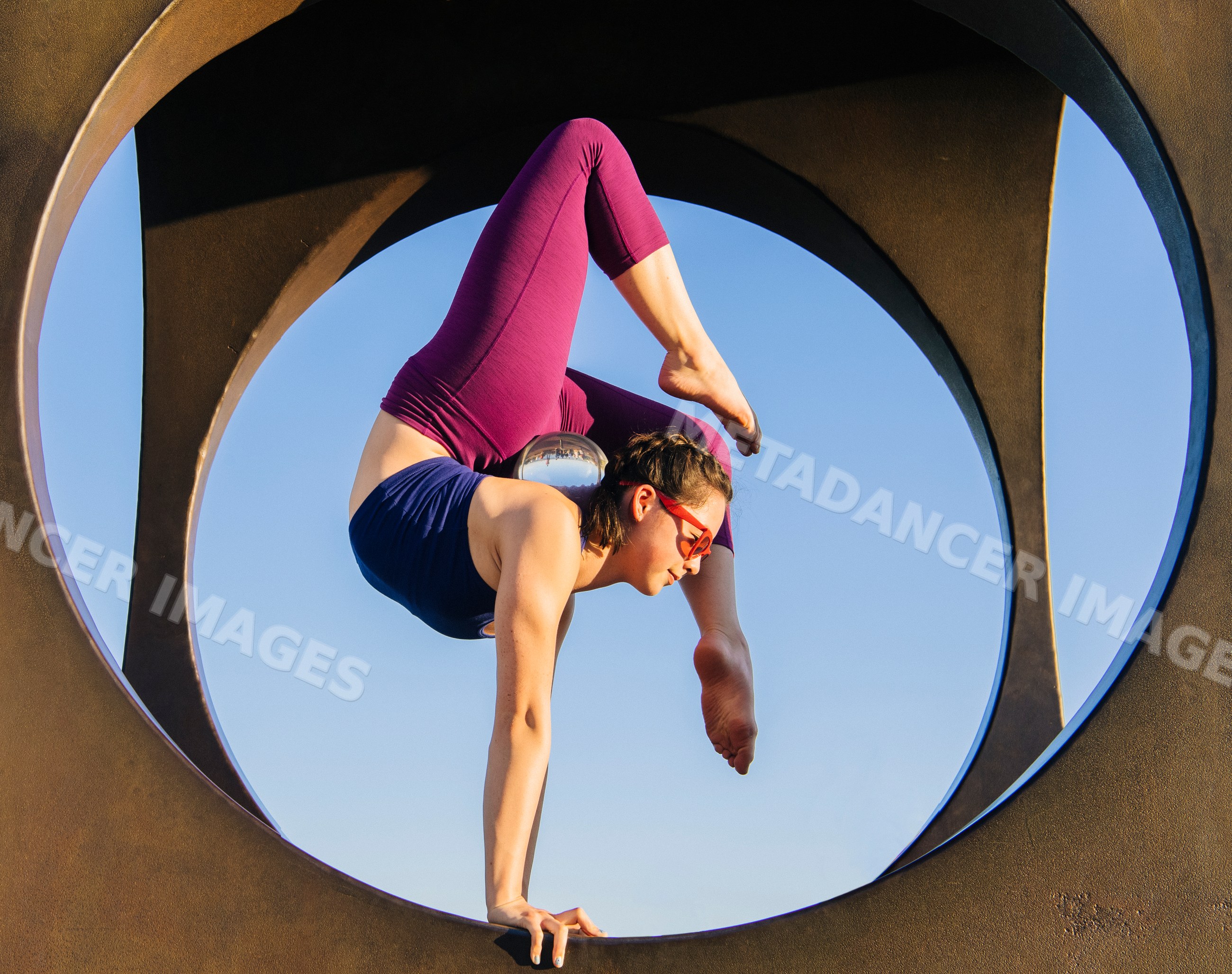 White woman performing yoga handstand inside circular outdoor frame