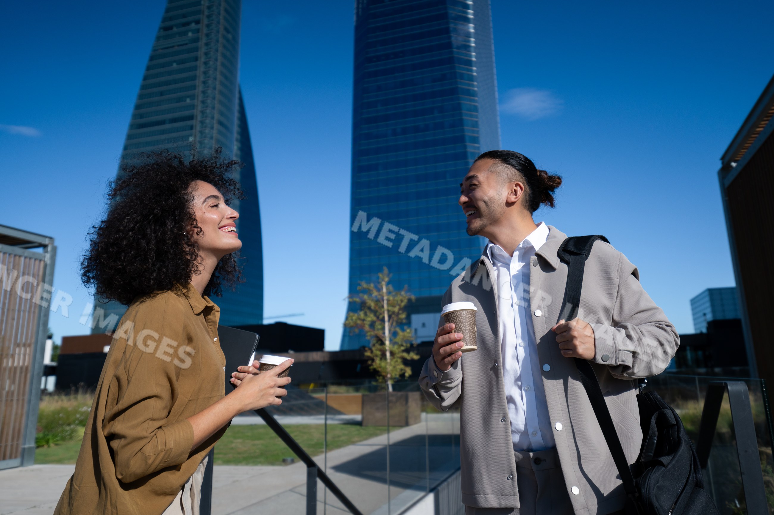 Two young professionals talking with coffee near skyscrapers in Madrid