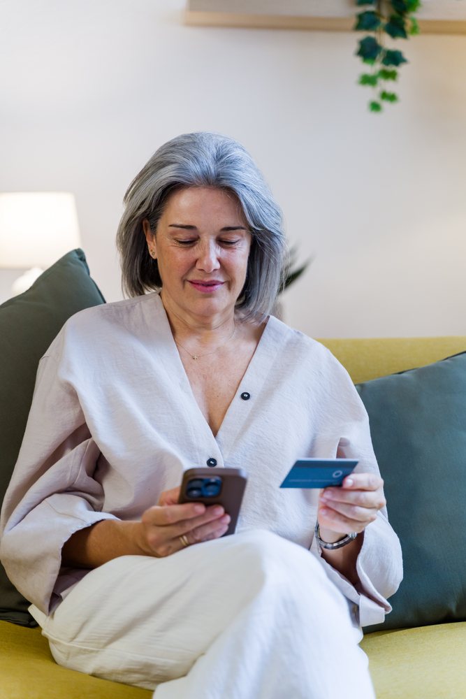 White woman shopping online with smartphone and credit card on sofa
