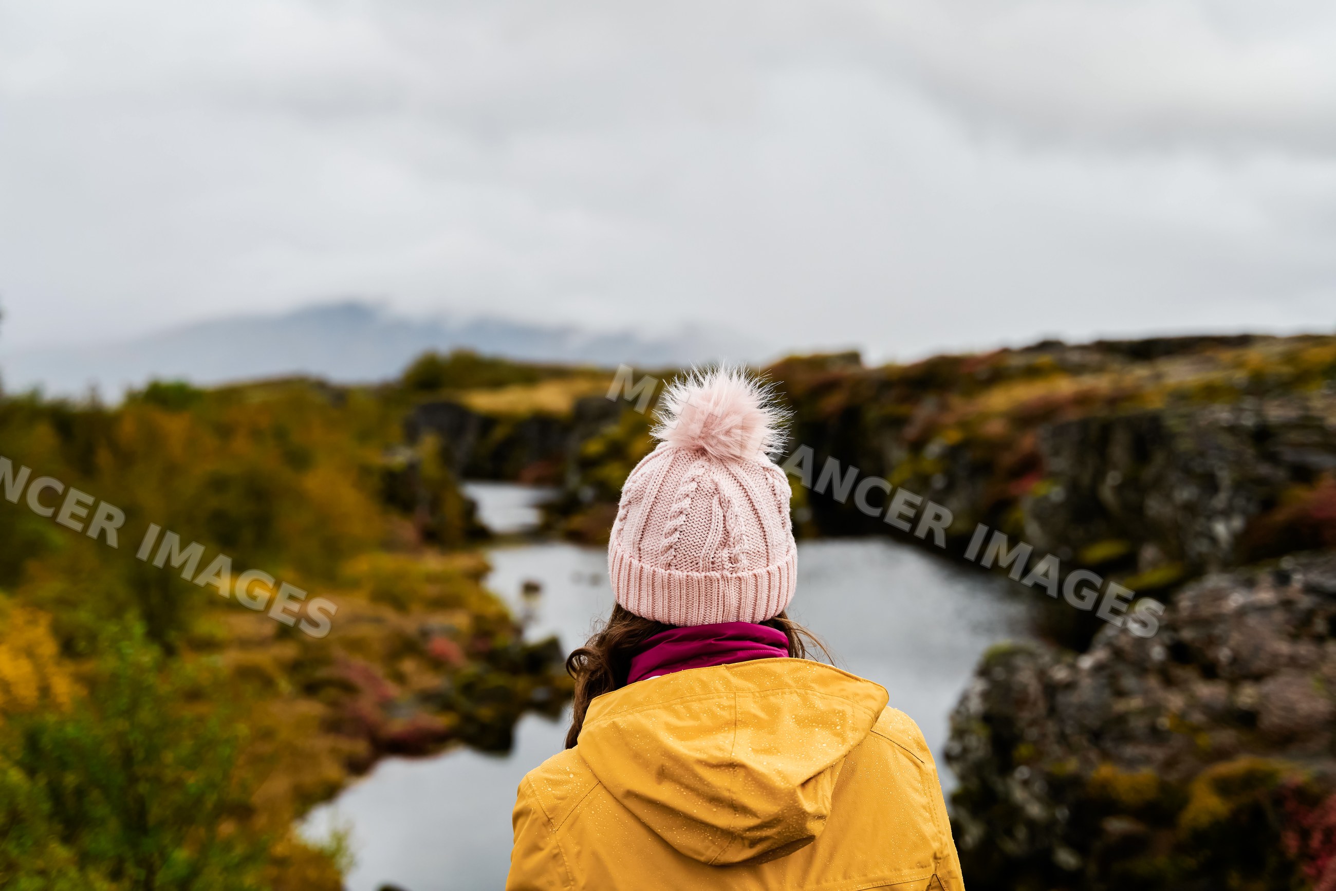 A white woman in a yellow jacket enjoys a misty autumn river view