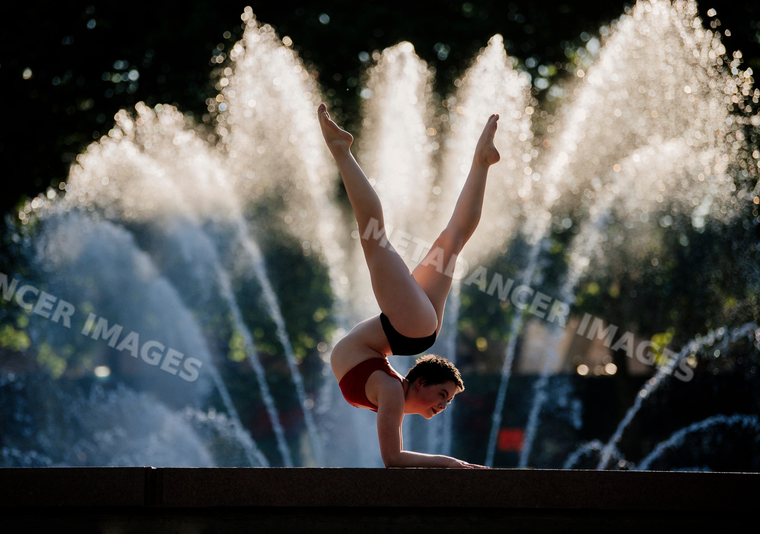 White person performing handstand yoga pose with water fountain