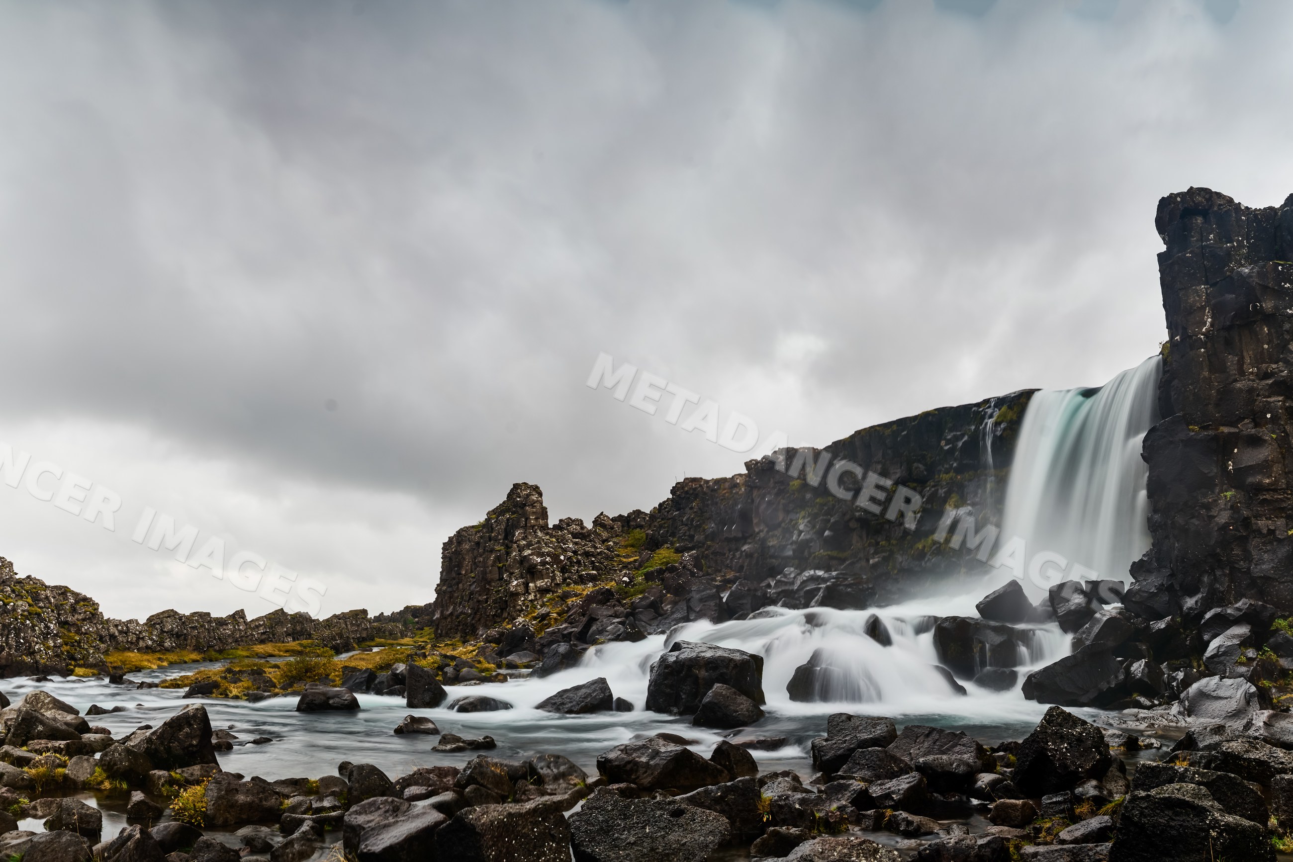 Waterfall cascading over rocky terrain under cloudy sky