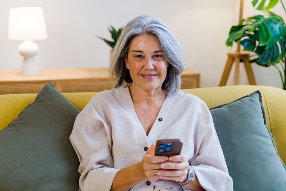 White woman sitting on yellow couch holding smartphone in living room